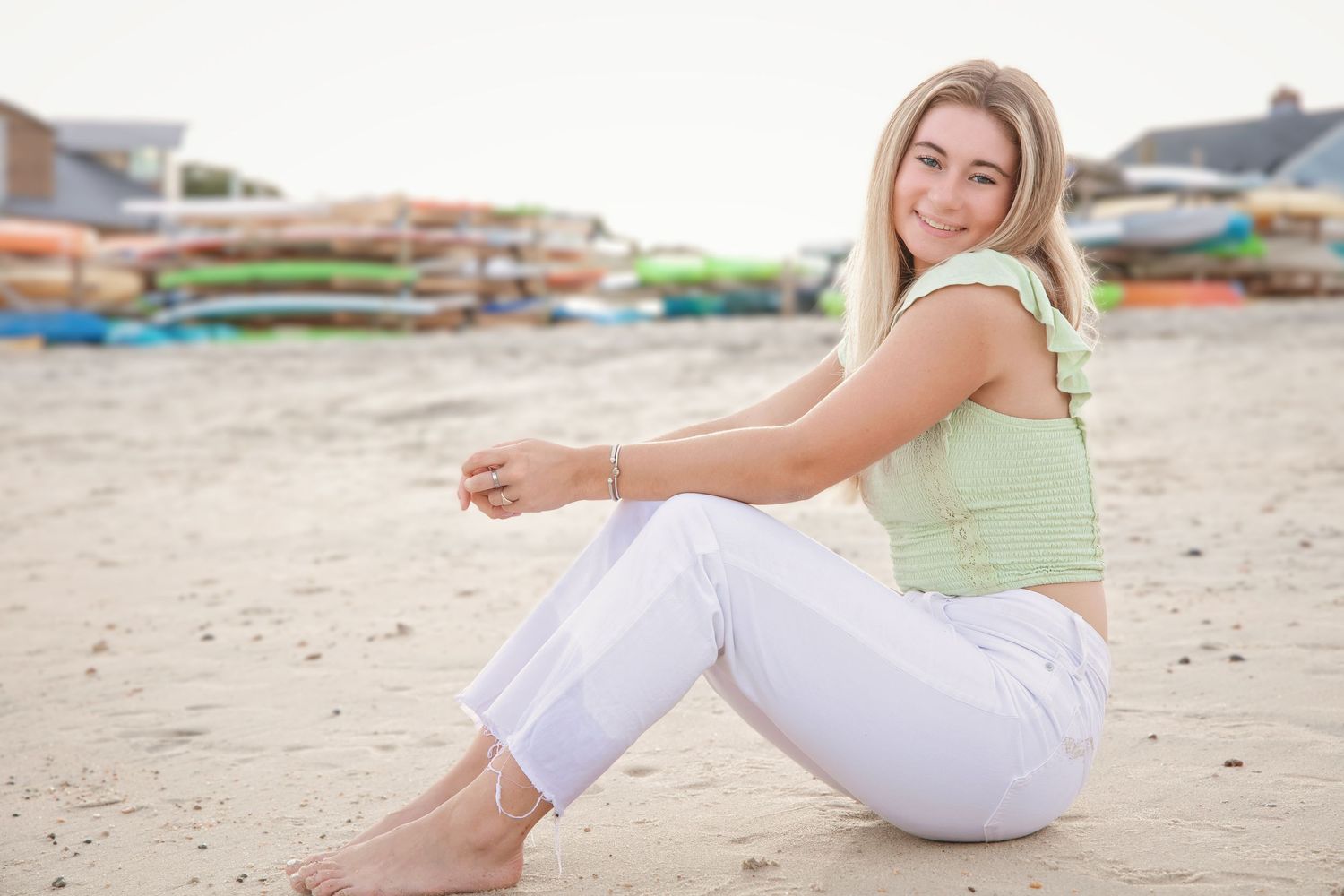Person in white outfit relaxing on sandy beach during summer photoshoot at sunset.