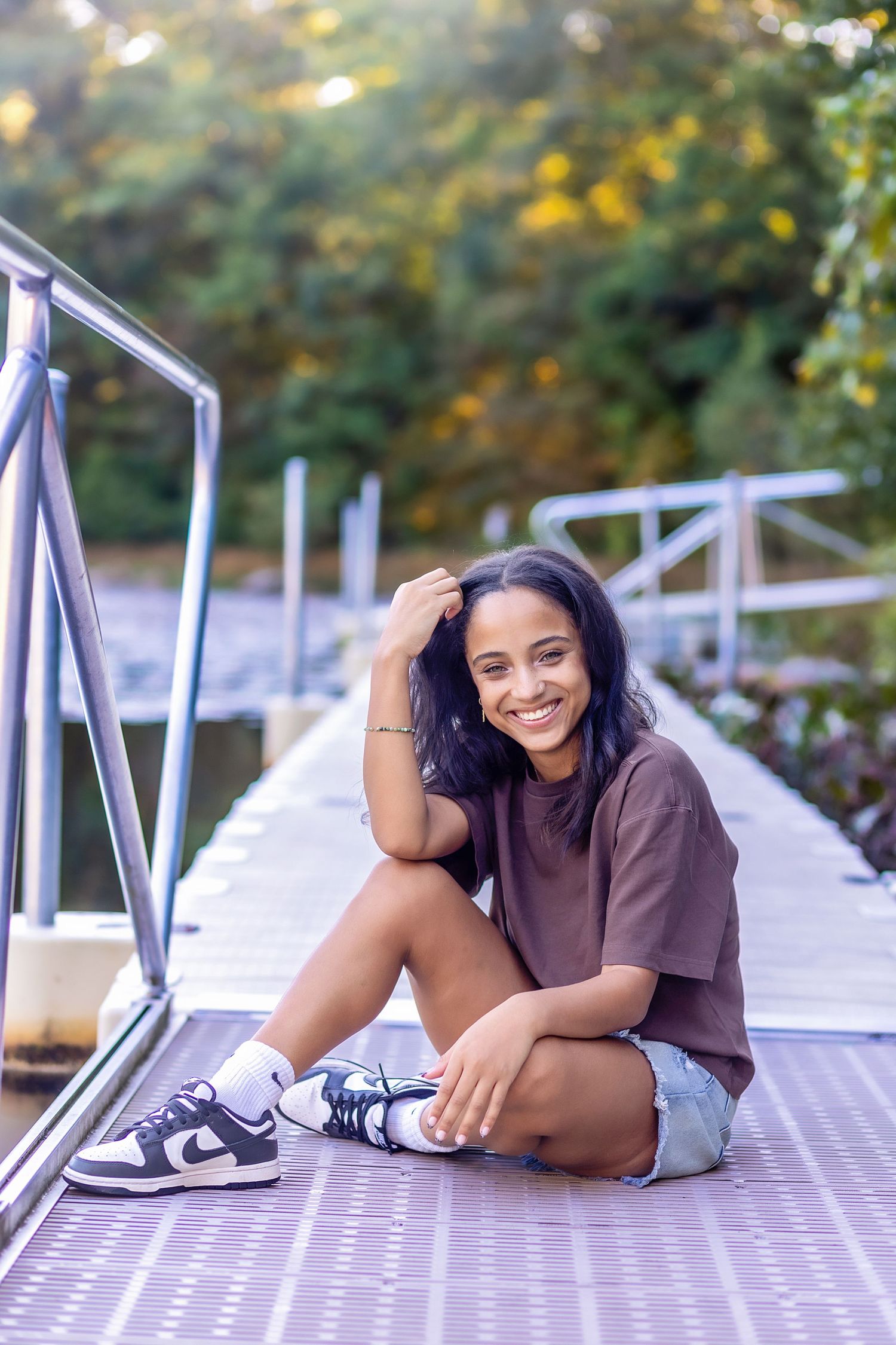 A person in a brown shirt lies casually on a wooden deck with sneakers on their feet in a relaxed outdoor setting.