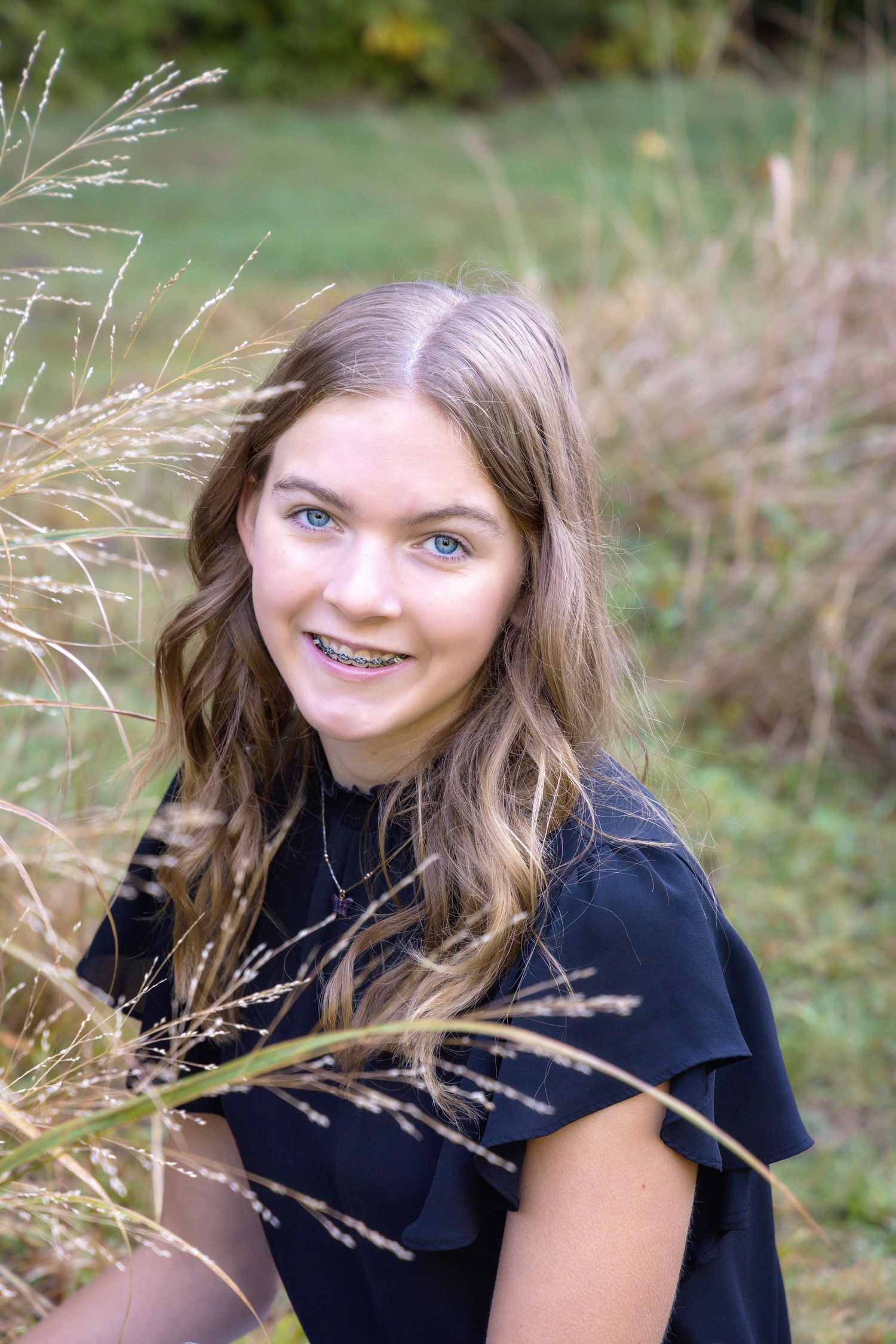 A series of outdoor portrait photos showing someone in a black top sitting in tall grass and wildflowers.