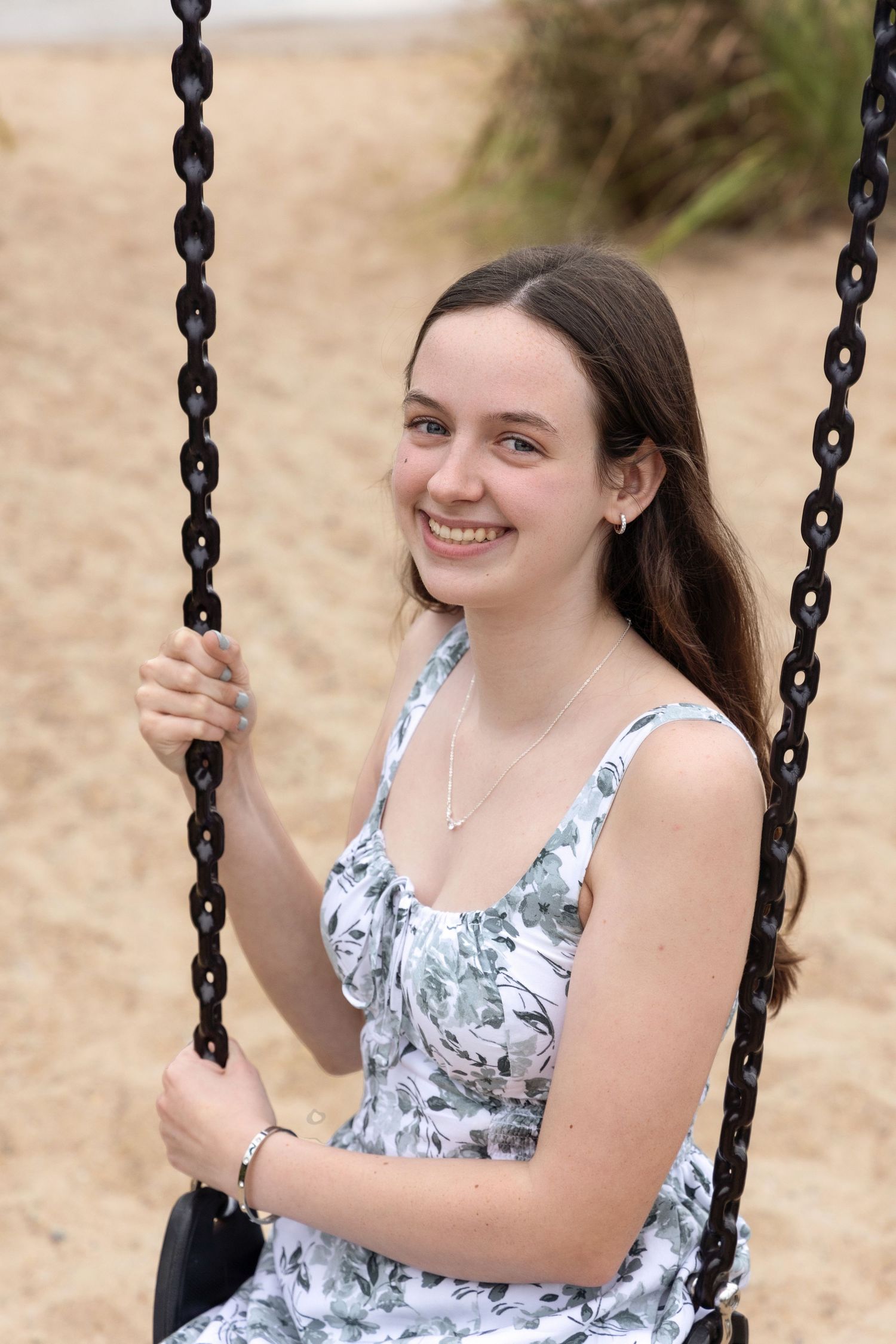 A person in a floral print top smiling while sitting on a playground swing on a sunny day.