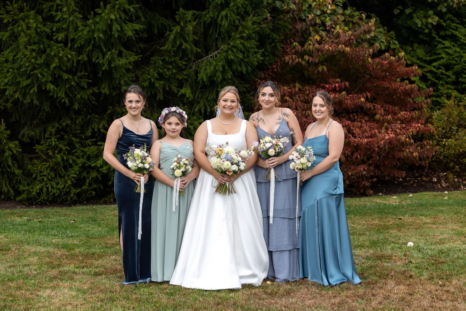 Bridesmaids in varying shades of blue dresses pose with bride holding bouquets.