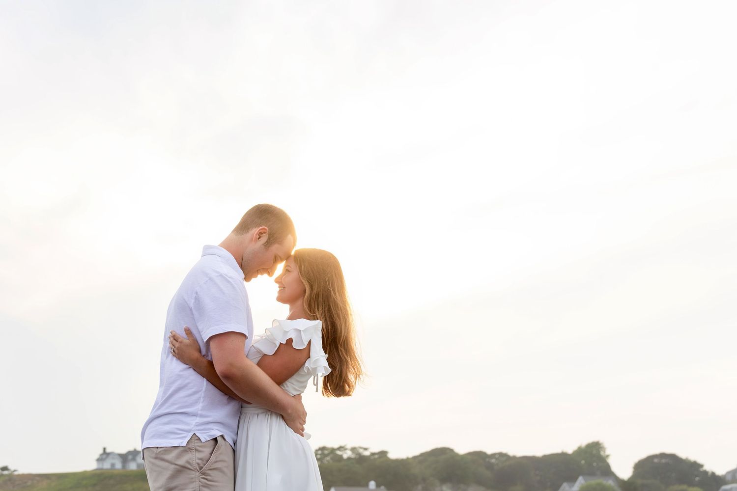 A romantic couple embraces on a beach during sunset, silhouetted against the orange and pink sky.