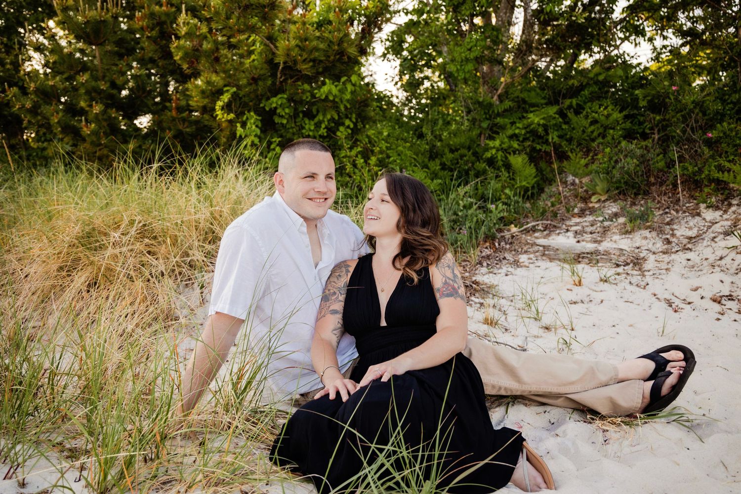 A romantic couple sits together on a sandy beach during golden hour.