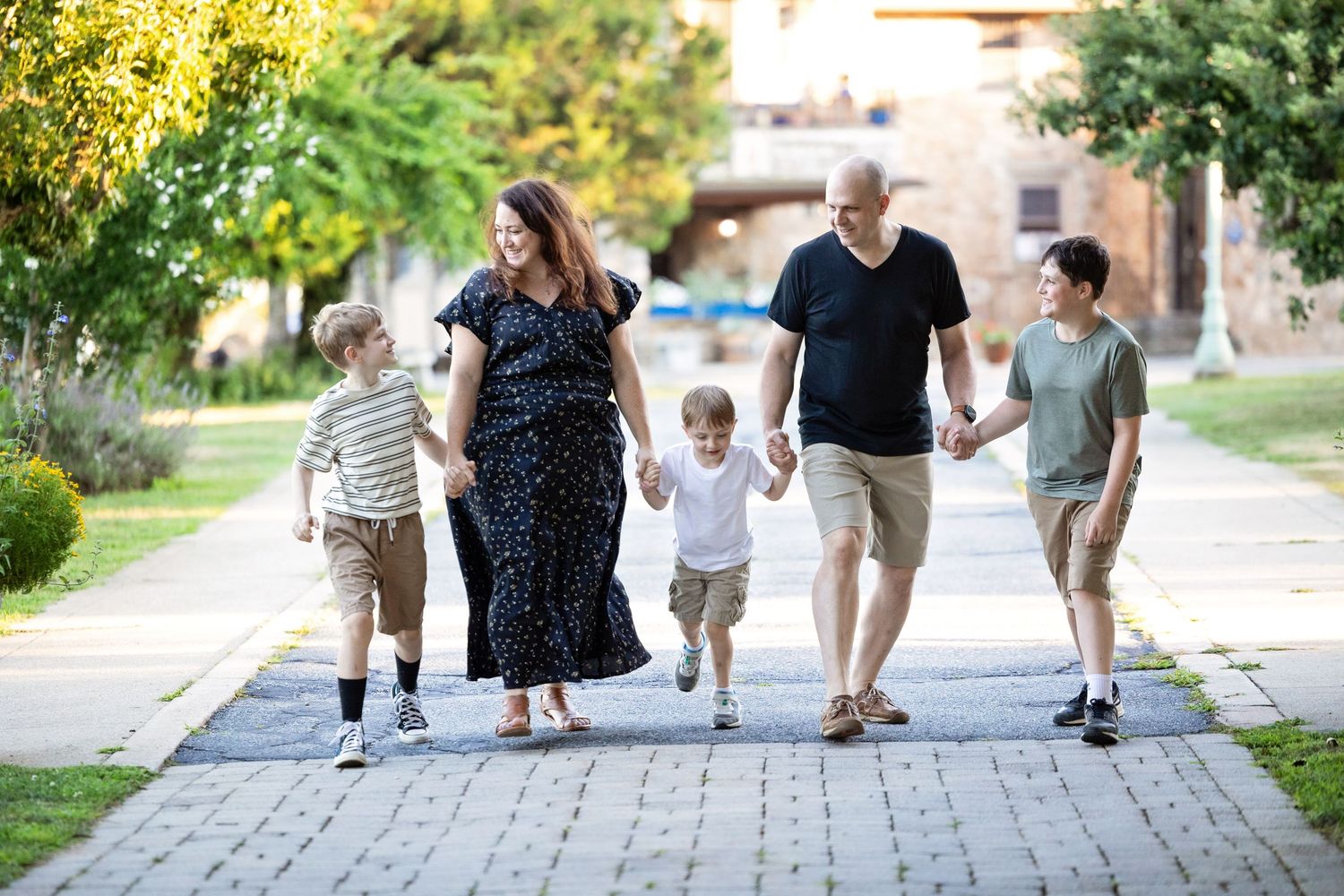 A family walks together on a paved pathway surrounded by greenery on a sunny day.