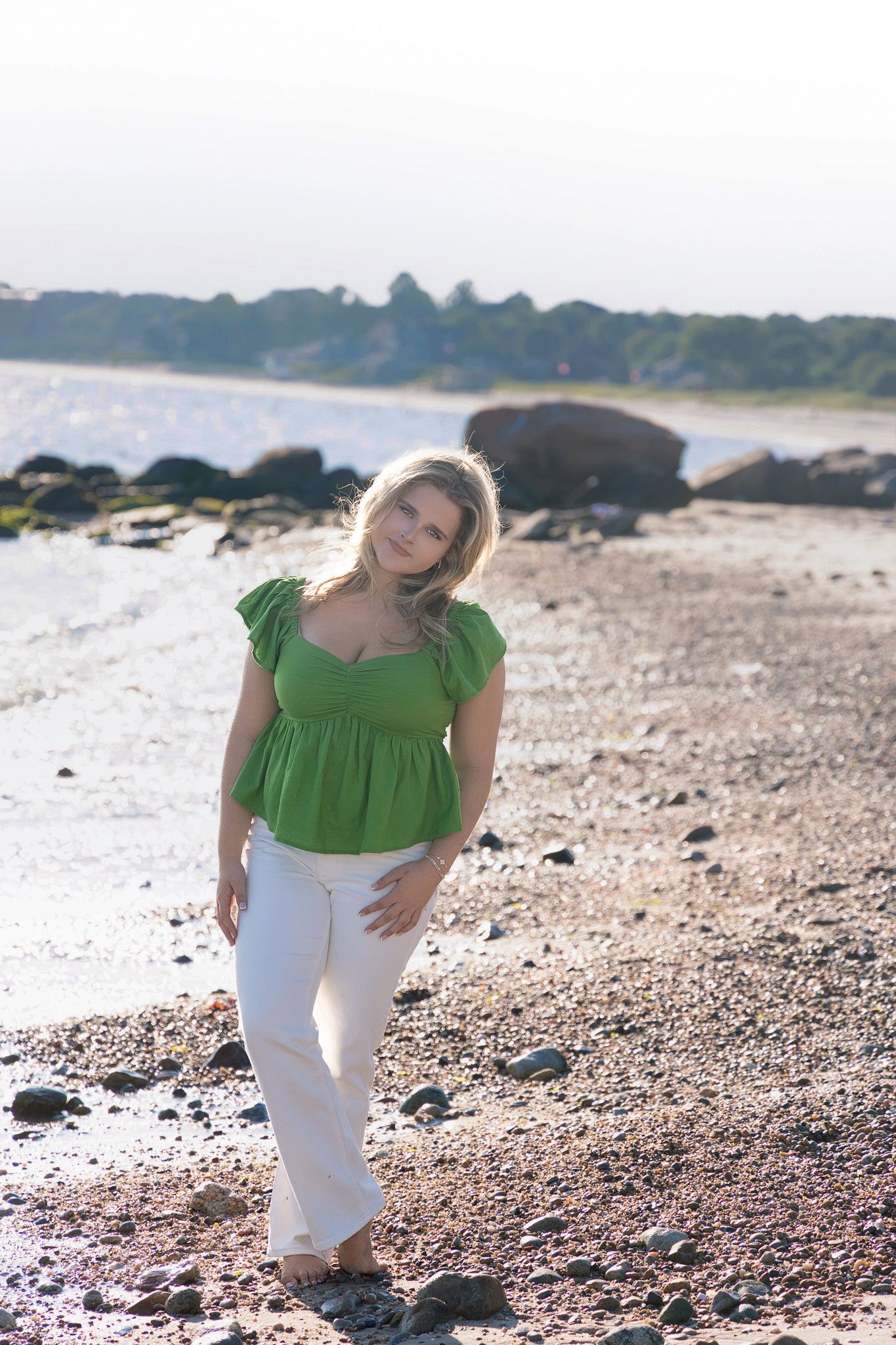 Beach photoshoot wearing green top and white pants on rocky shoreline.