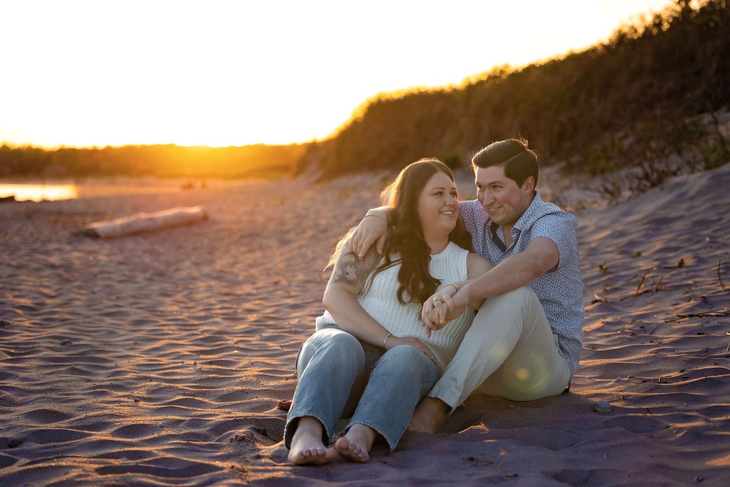 Couple sitting together on sandy beach during golden sunset creating silhouettes against orange sky.