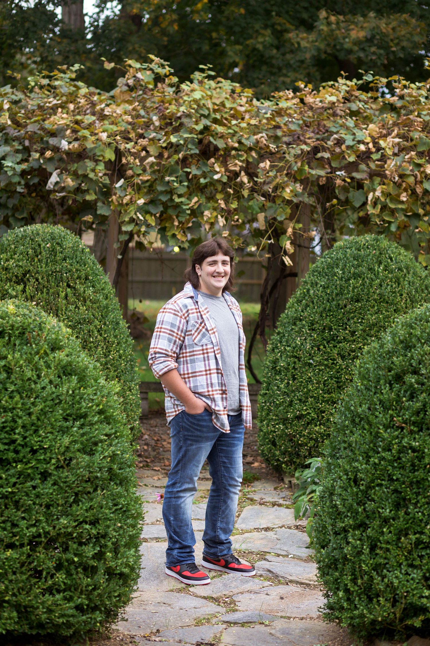 A garden path lined with neatly trimmed boxwood shrubs leads through autumn foliage.