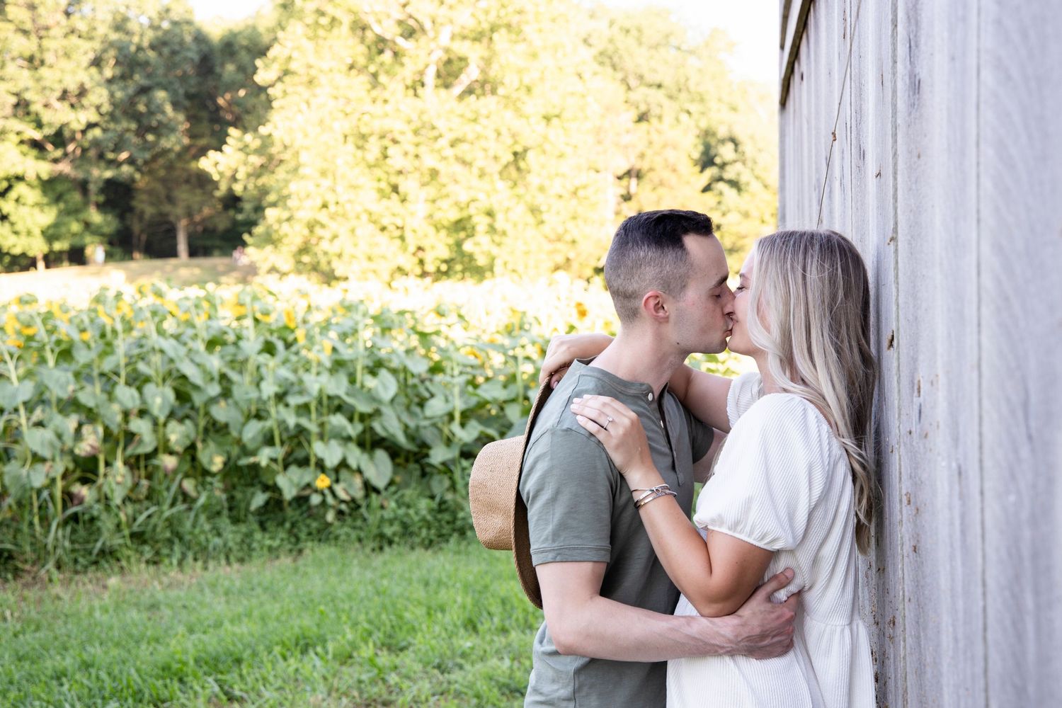 A romantic couple shares tender moments against a sunlit outdoor backdrop with trees and greenery.