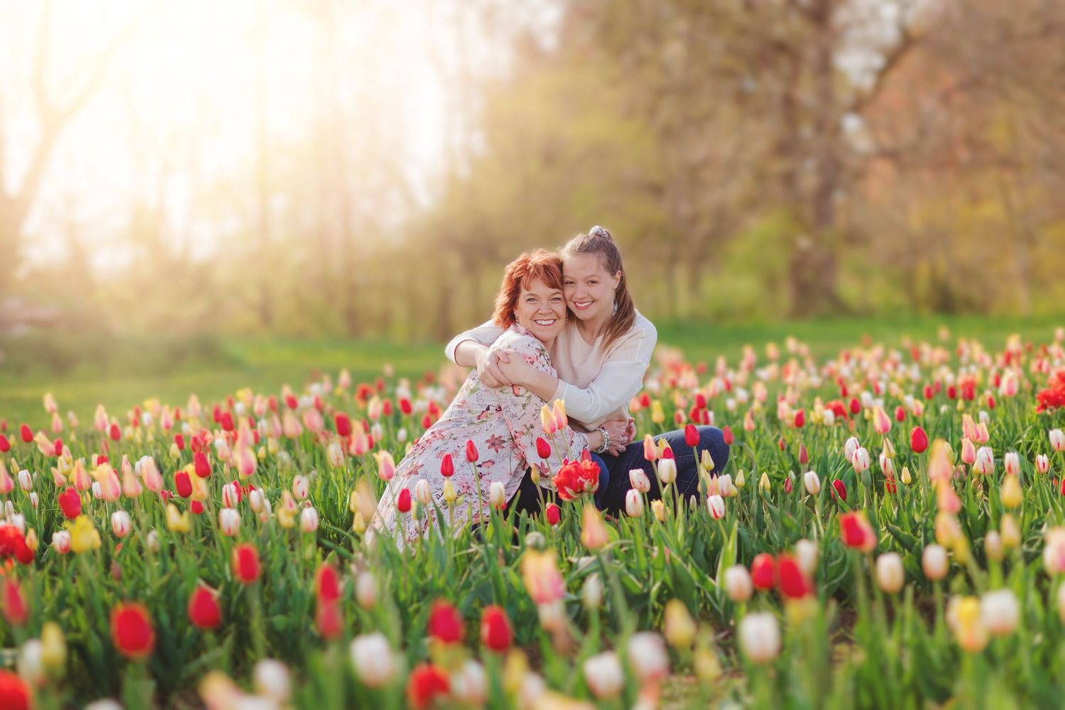 Two people share a tender moment among vibrant red and yellow tulips in a spring garden during golden hour.