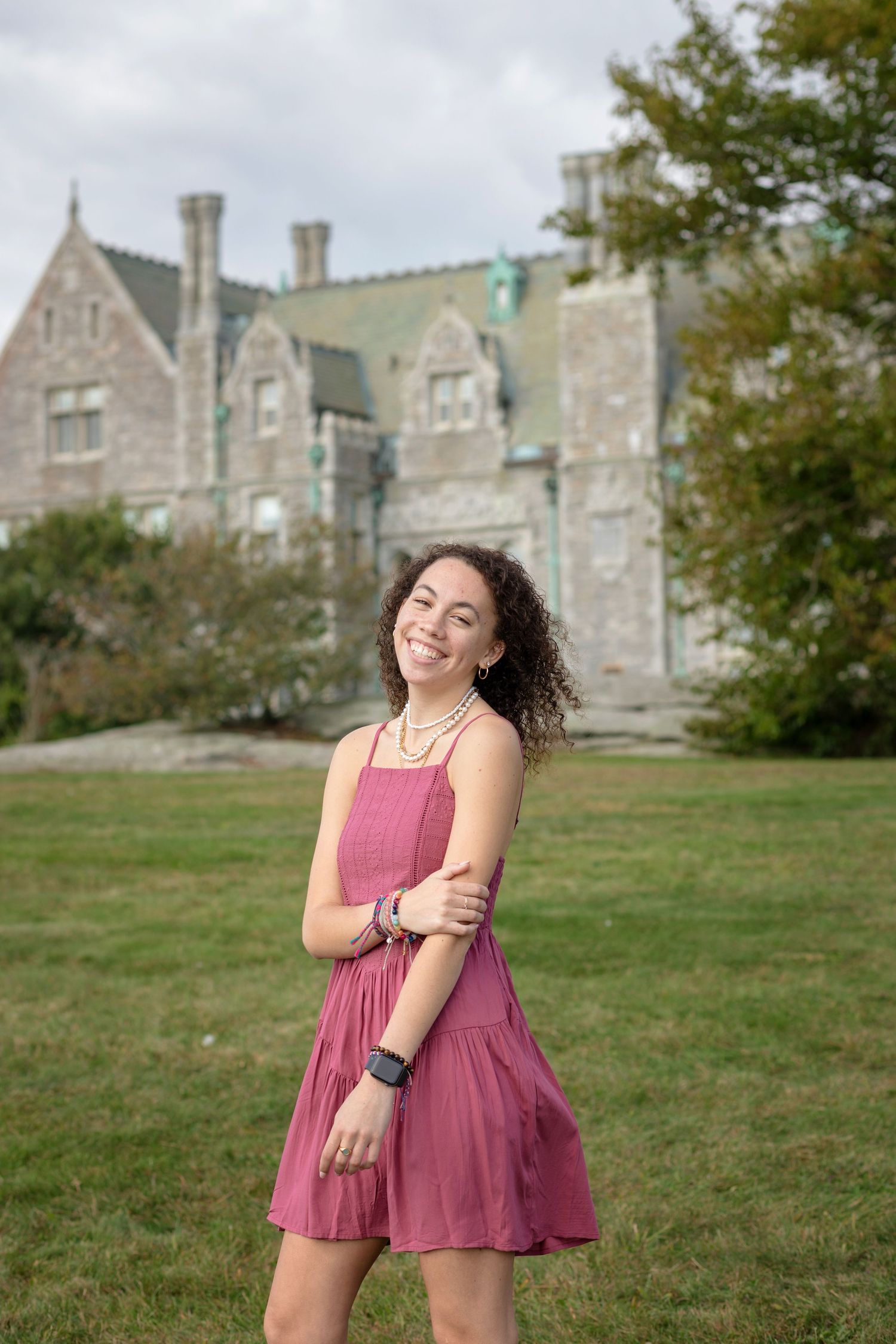 A person in a flowing mauve dress dances and twirls playfully on a grassy lawn with a stone castle in the background.