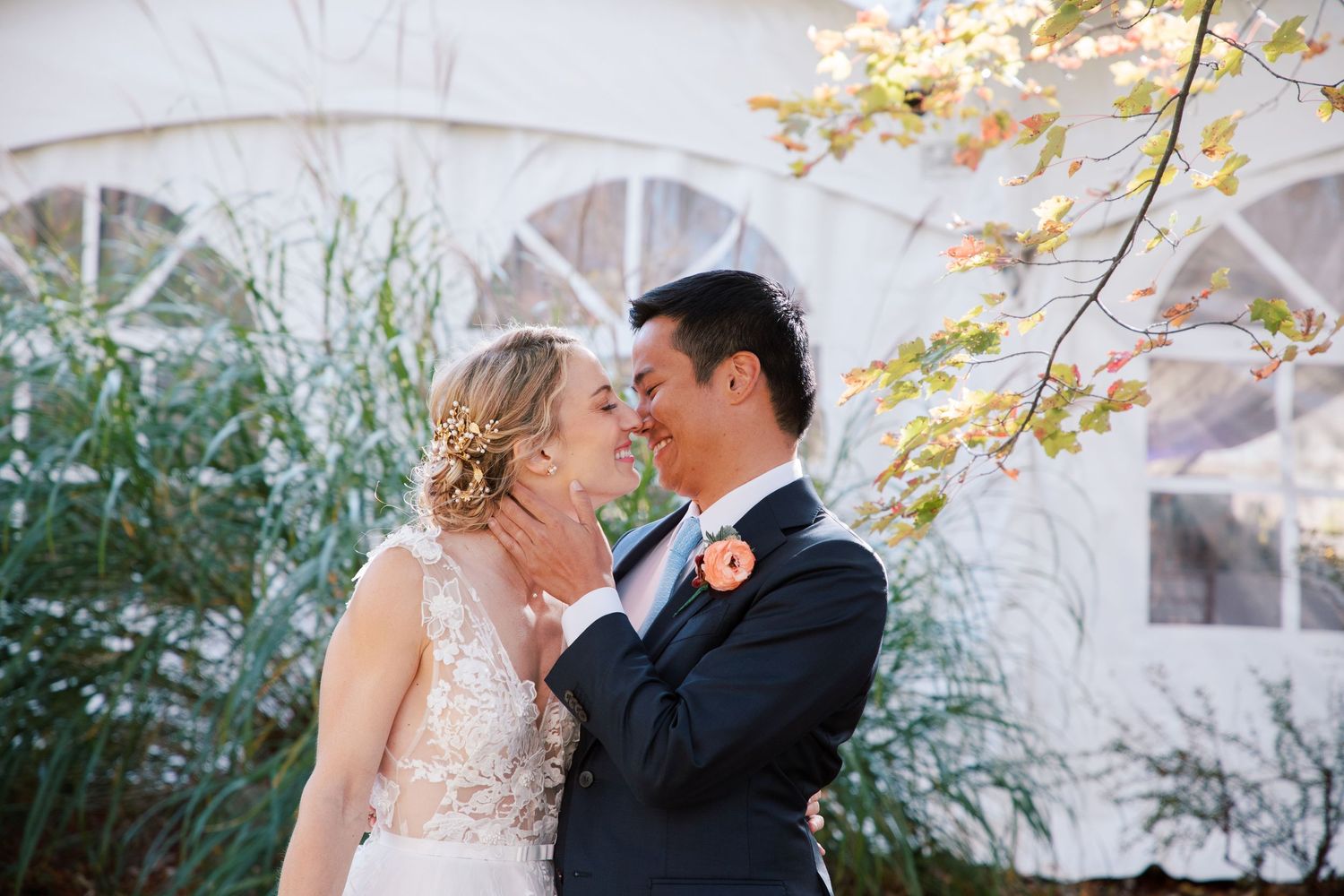 Couple in formal wedding attire sharing romantic moments in an outdoor garden setting with autumn foliage.