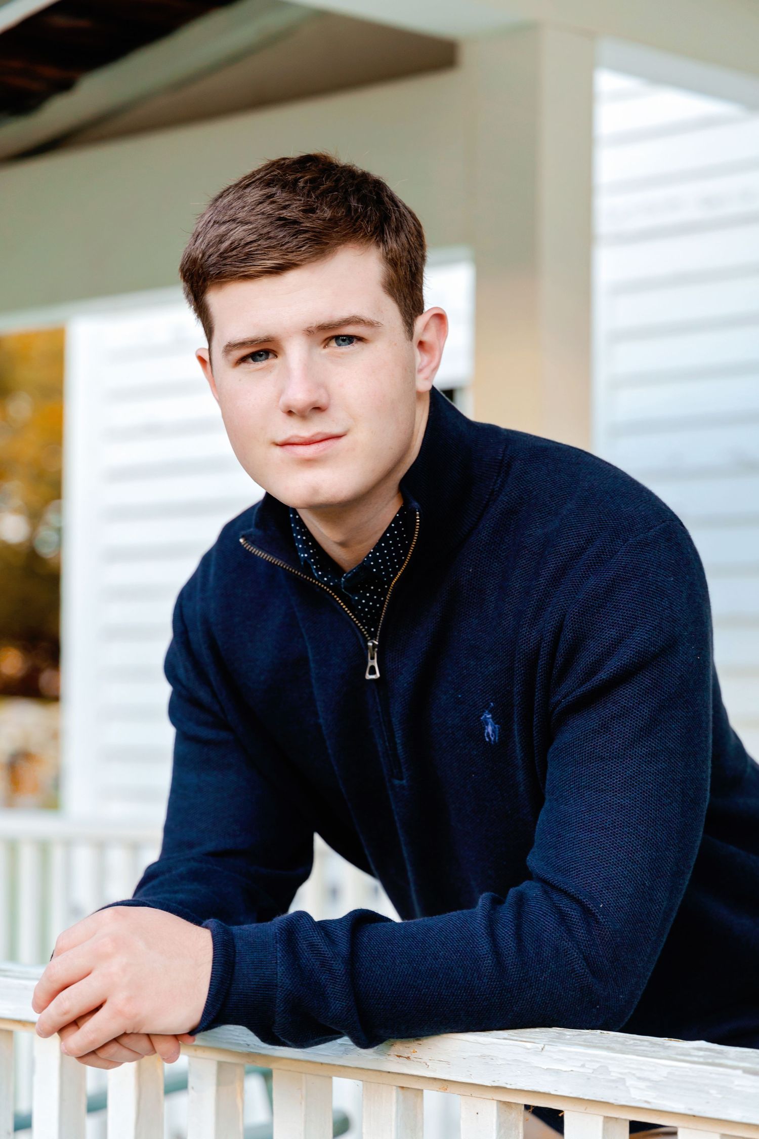 A person in a navy blue zip-up sweater leans on a white railing in a bright indoor setting.