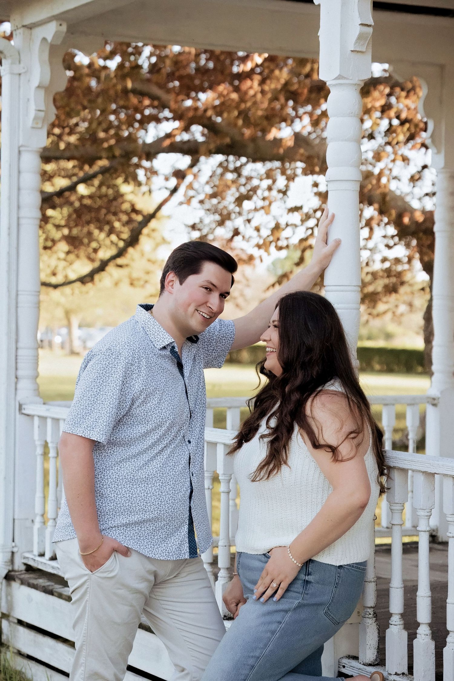 Couple laughing and embracing on white porch during romantic photo session at sunset.
