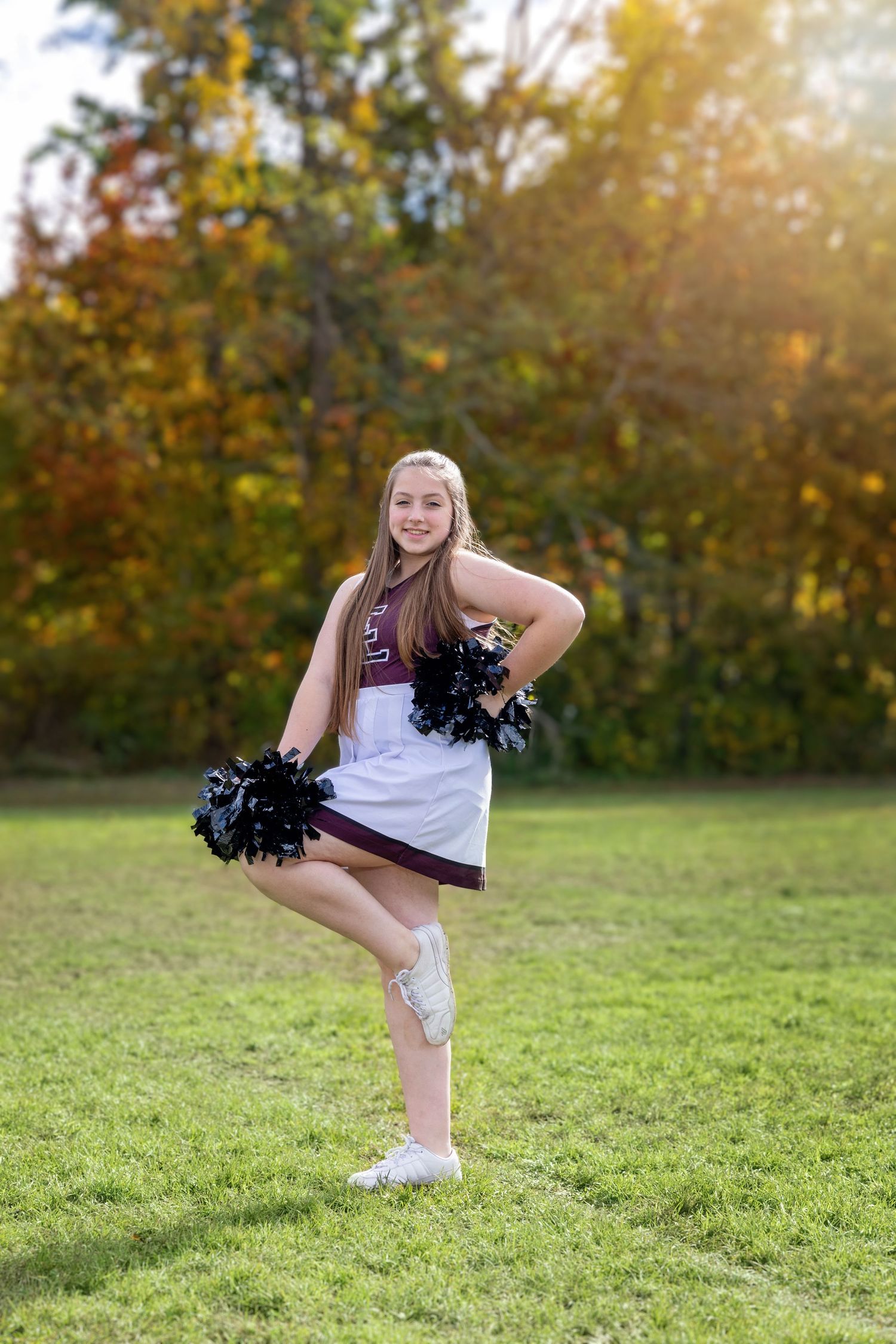 Young cheerleader performs high kick on grassy field during golden autumn sunset.