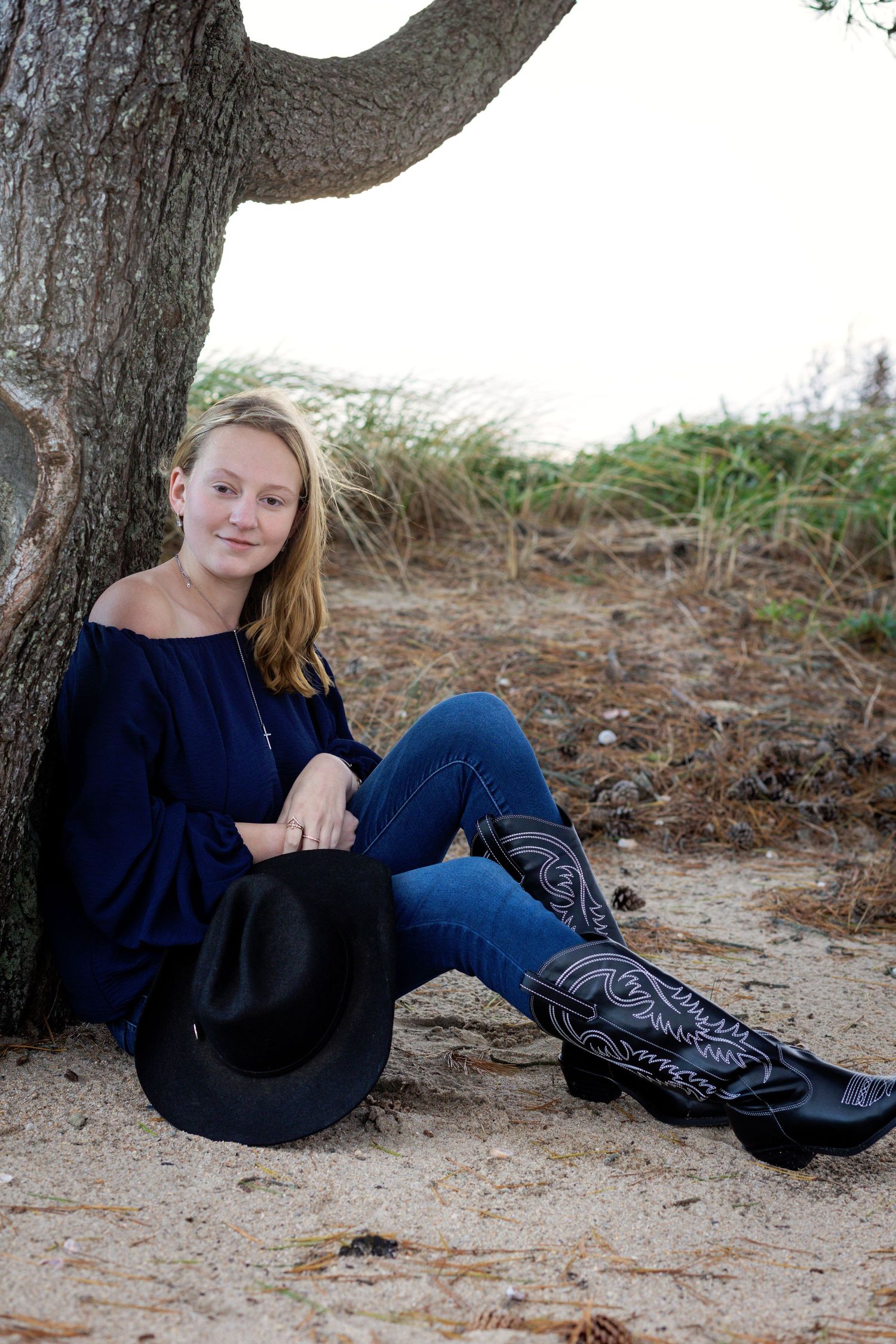 A person in a navy sweater and jeans reclines on the ground beneath a tree in an outdoor setting.