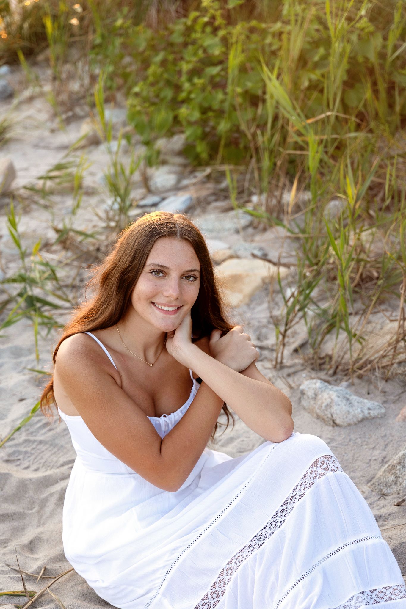 A flowing white lace dress stands out against natural beach vegetation and sand dunes.