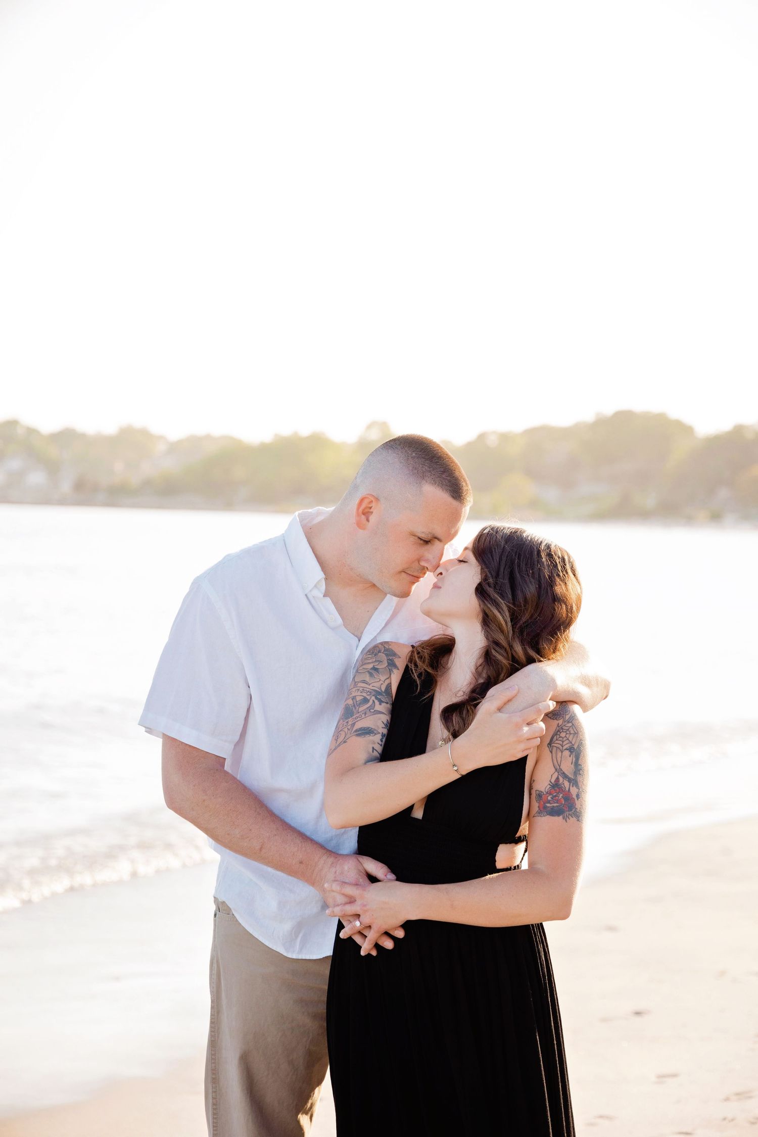 A romantic couple shares an intimate moment at sunset on a sandy beach with golden light glowing behind them.