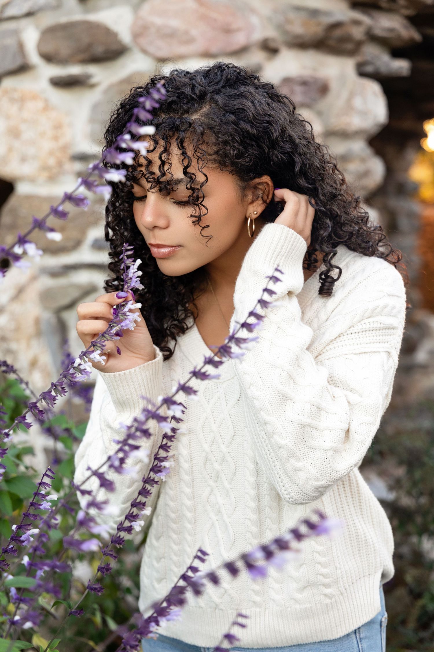 Artistic portrait with purple lavender flowers against a stone wall background.