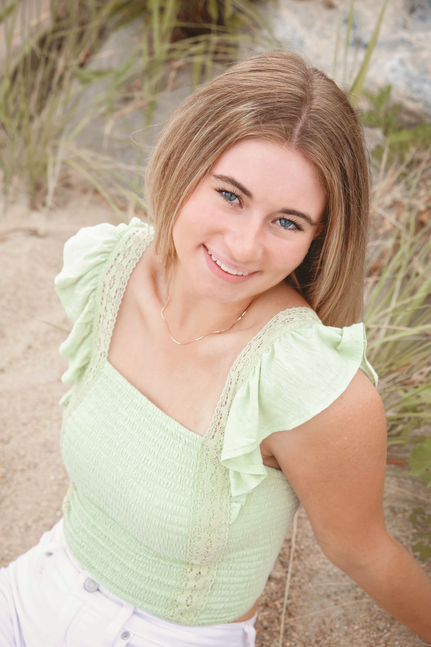 A portrait in soft lighting shows someone wearing a mint green ruffled top against a natural beach backdrop.