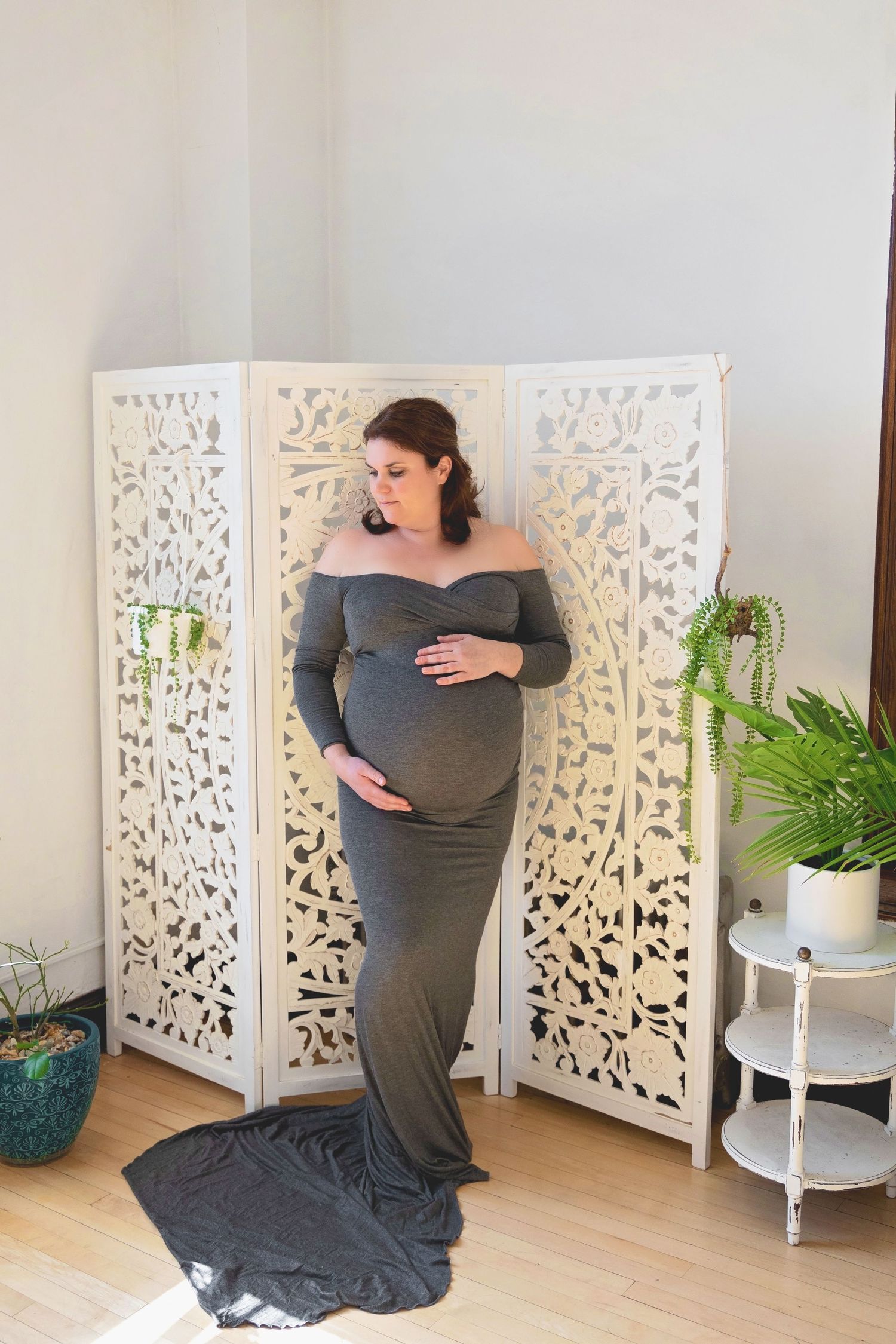 A person in a gray dress demonstrates four different yoga positions on a hardwood floor next to white decorative screens.