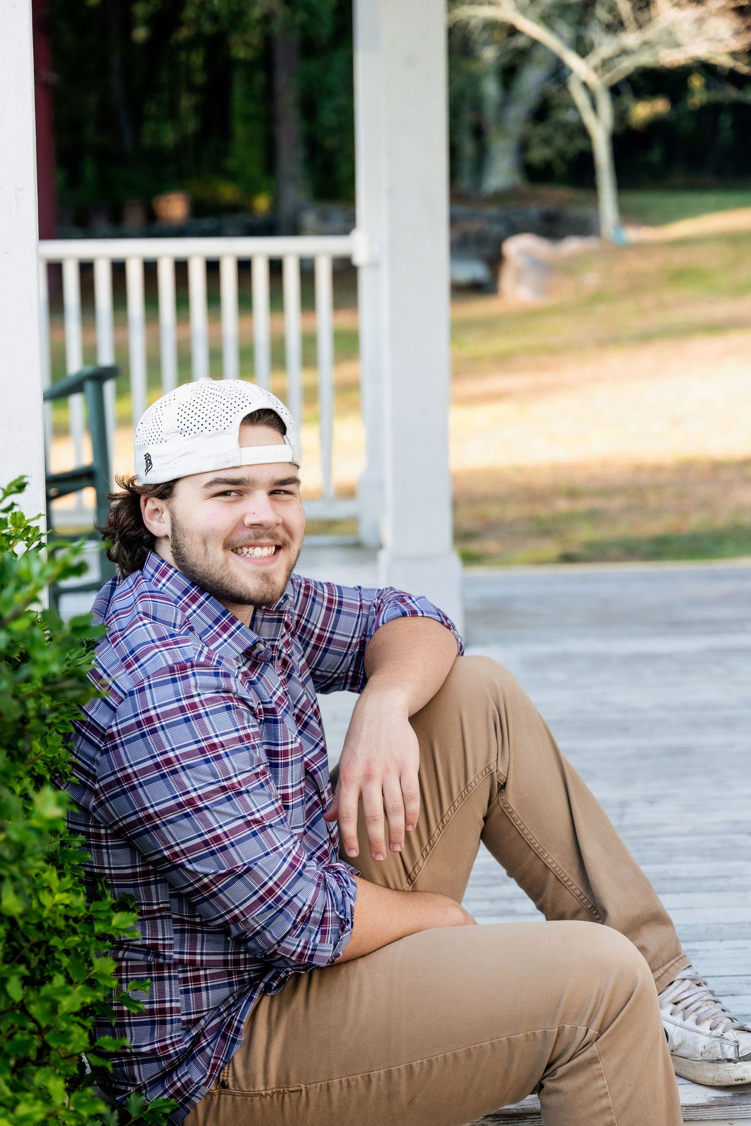 A person in a plaid shirt and khaki pants sits casually on outdoor steps in a garden setting.