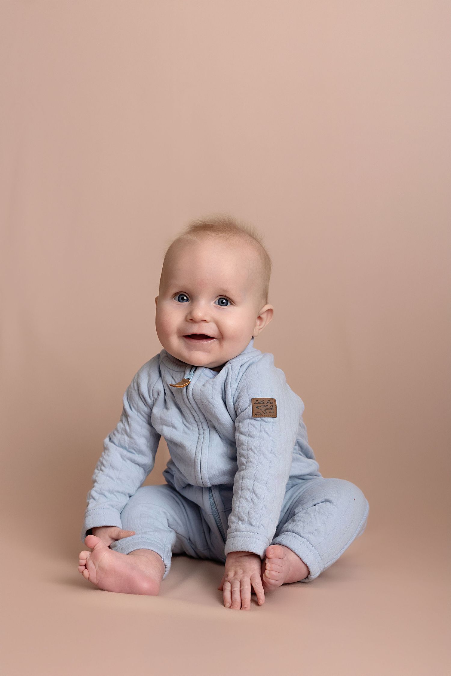 Baby in light blue quilted outfit crawls and plays on beige backdrop in progressive milestone photo series.