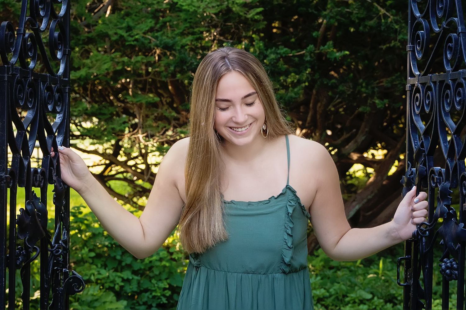 A person in a green dress poses playfully in front of lush garden foliage on a sunny day.