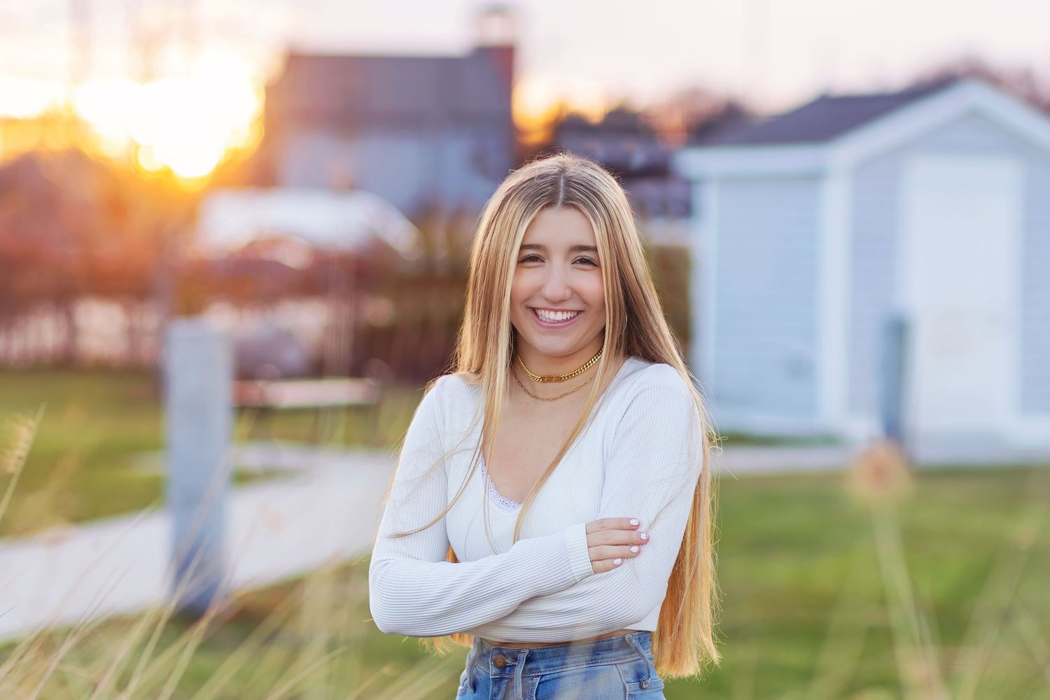 A woman in a white sweater laughs joyfully while posing outdoors during golden hour sunset.