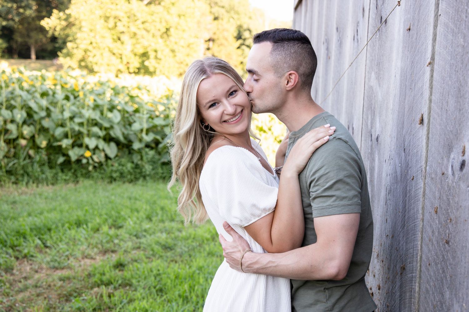 Romantic couple embraces against rustic wooden wall during outdoor engagement photo session in natural sunlight.