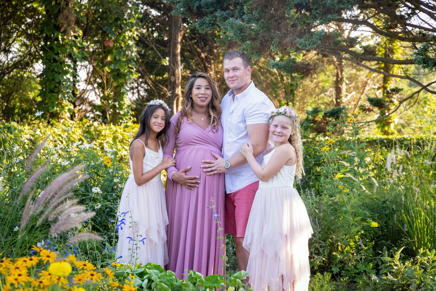A family poses together outdoors in coordinated pink and white outfits during a golden sunset photo session.