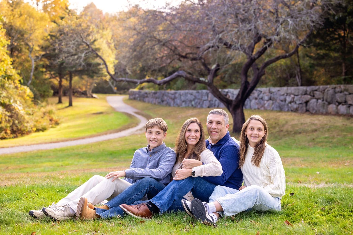 A group in casual attire relaxes together on a grassy hillside during a warm autumn afternoon.