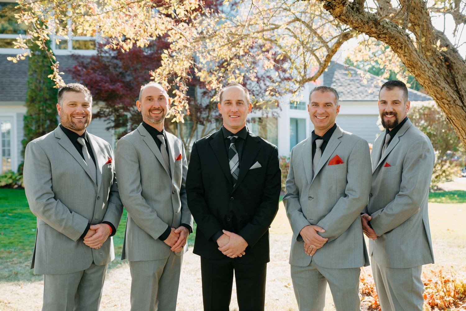 Wedding party in coordinated grey suits posing under blooming cherry tree.