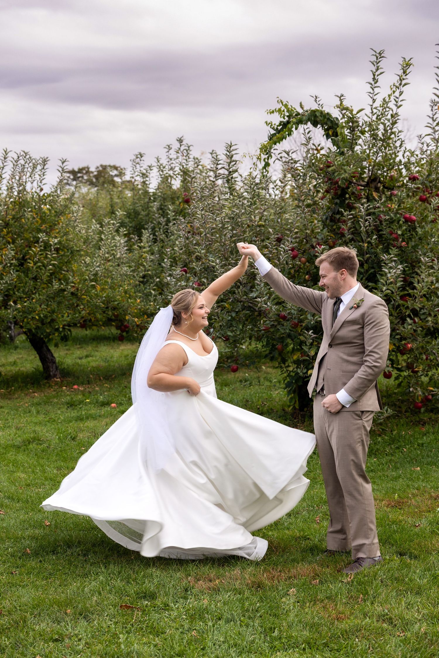 Couple dances in apple orchard as bride's dress twirls dramatically.
