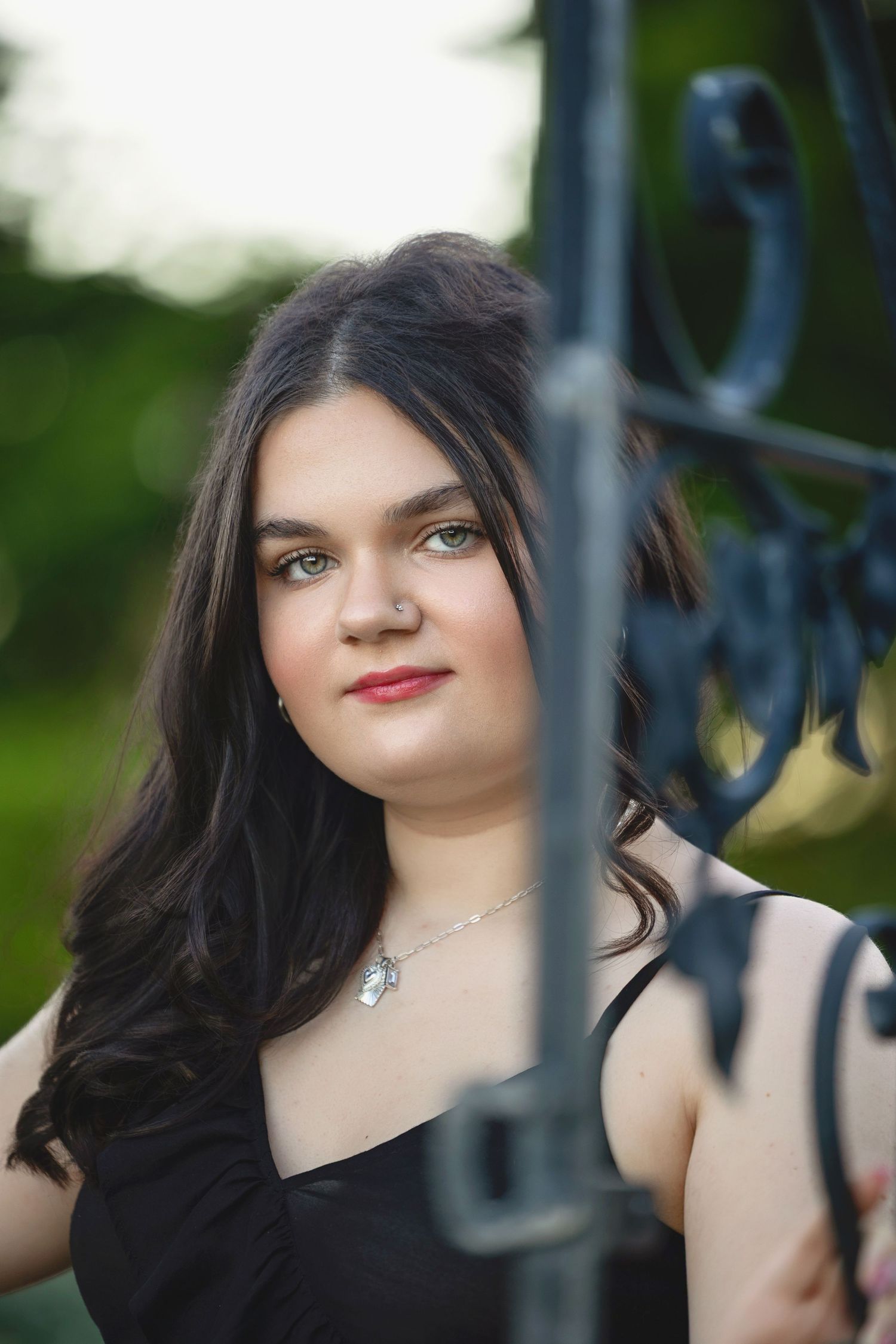 Portrait of someone in a black top posing against an ornate metal fence in a garden setting.