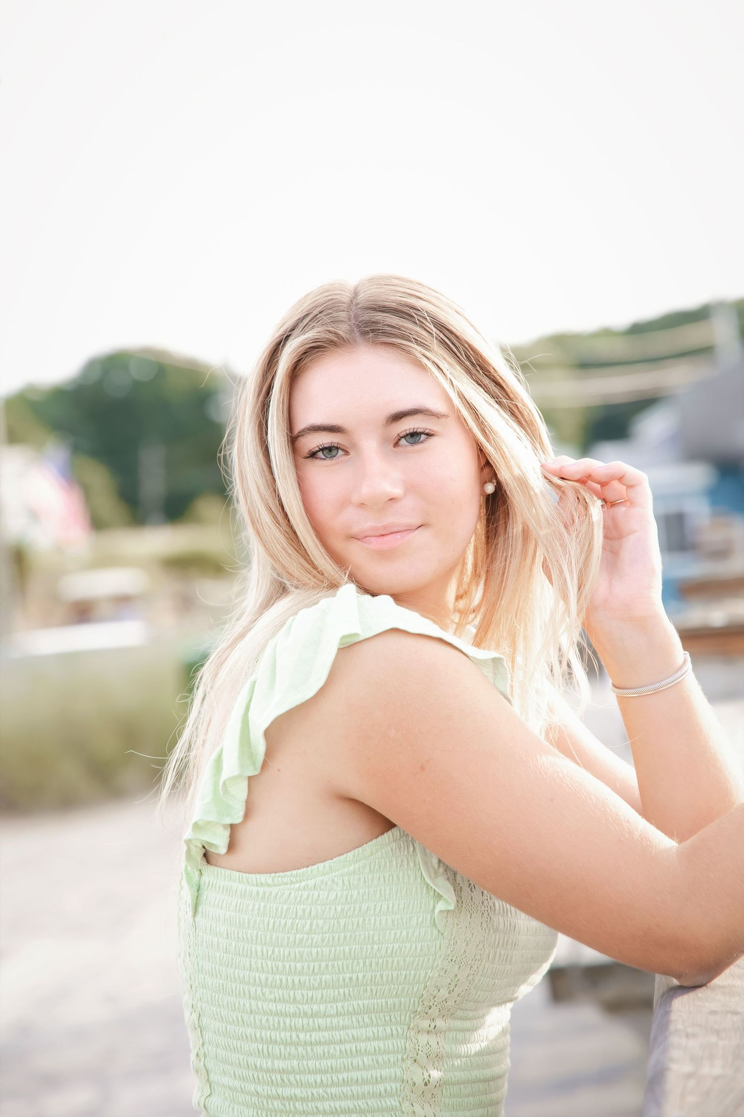 A person in a mint green summer top poses outdoors on a sunny day with a natural background.