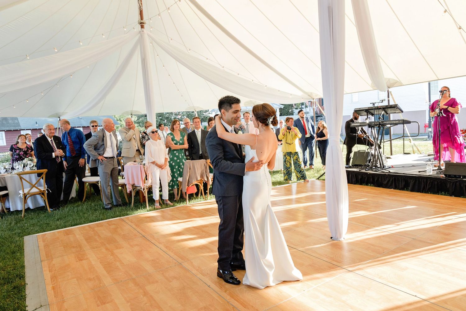 Couples dance together on a wooden floor under an elegant white tent during an outdoor wedding reception.
