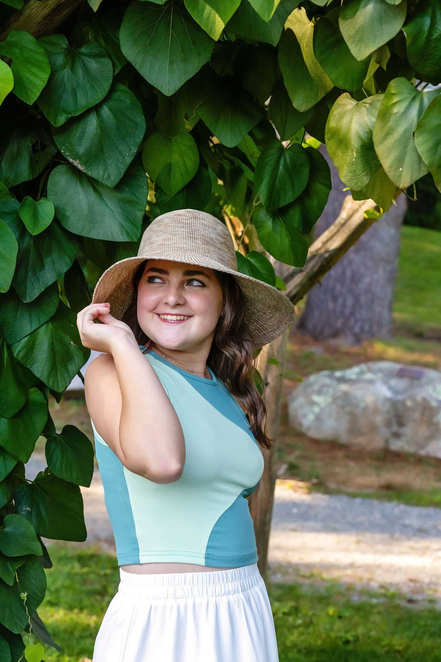 A person in a sun hat and turquoise top poses against lush green foliage in a garden setting.