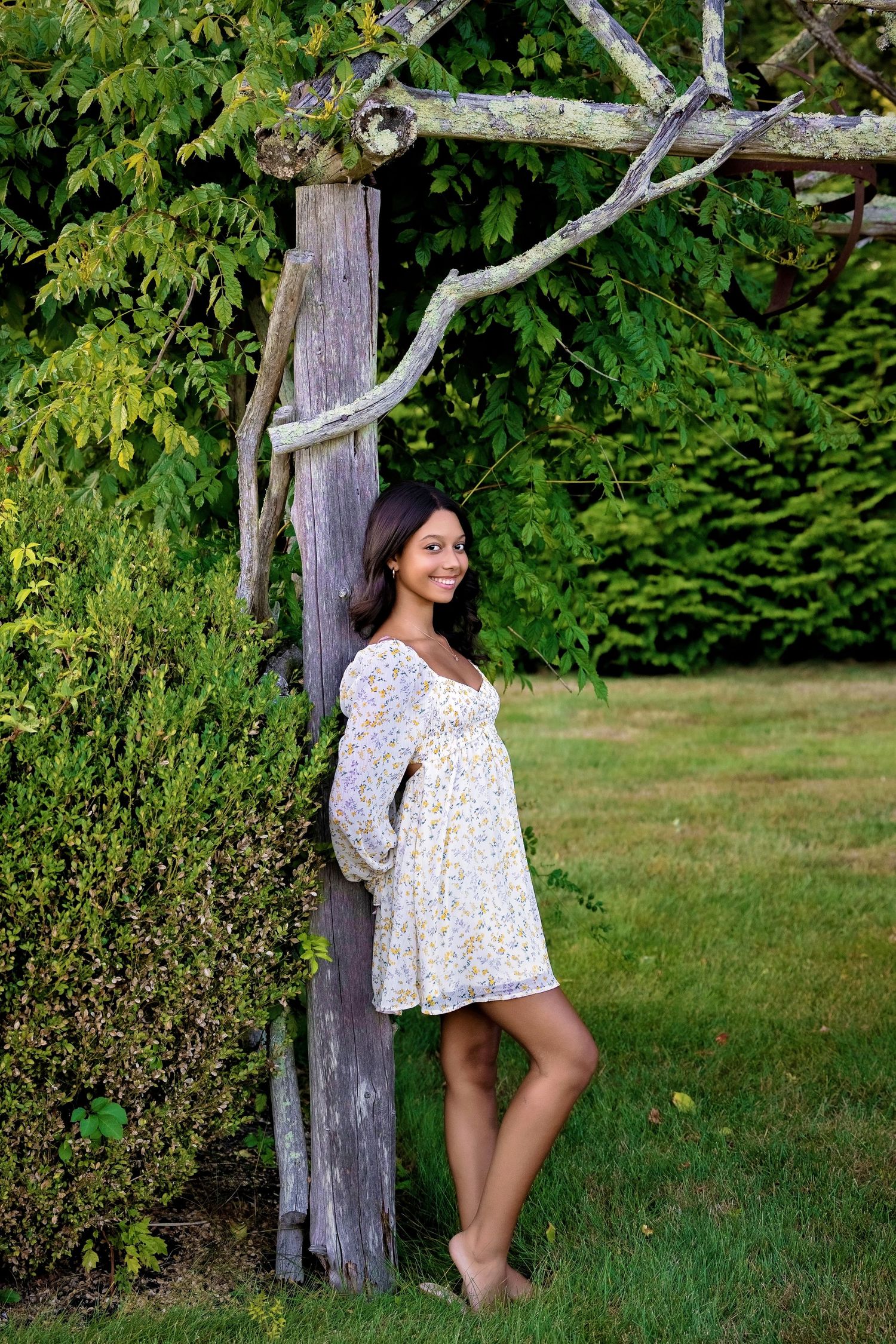 Summer portrait session against weathered wooden posts and green foliage.