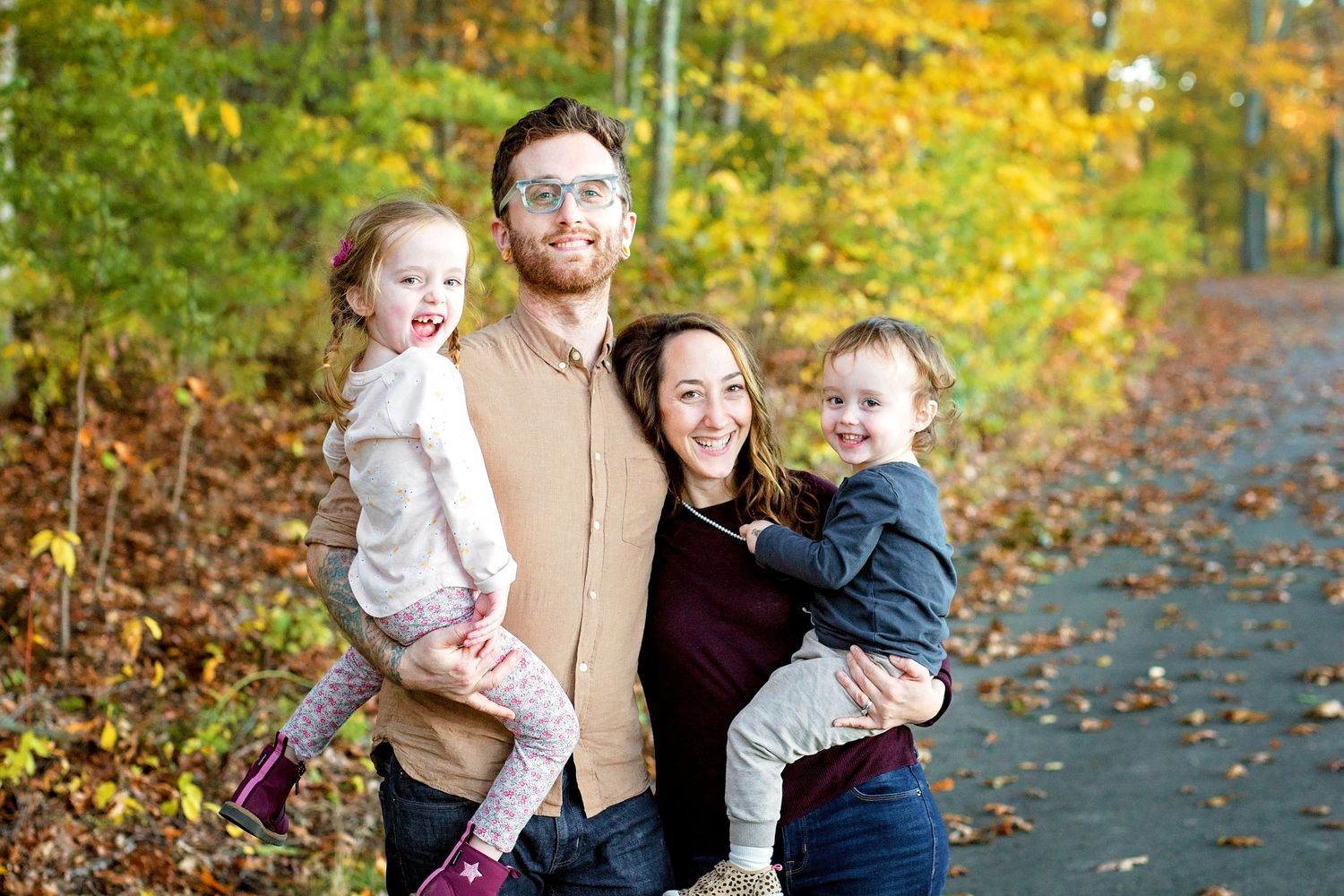 A family poses together on a path surrounded by vibrant fall foliage and scattered autumn leaves.