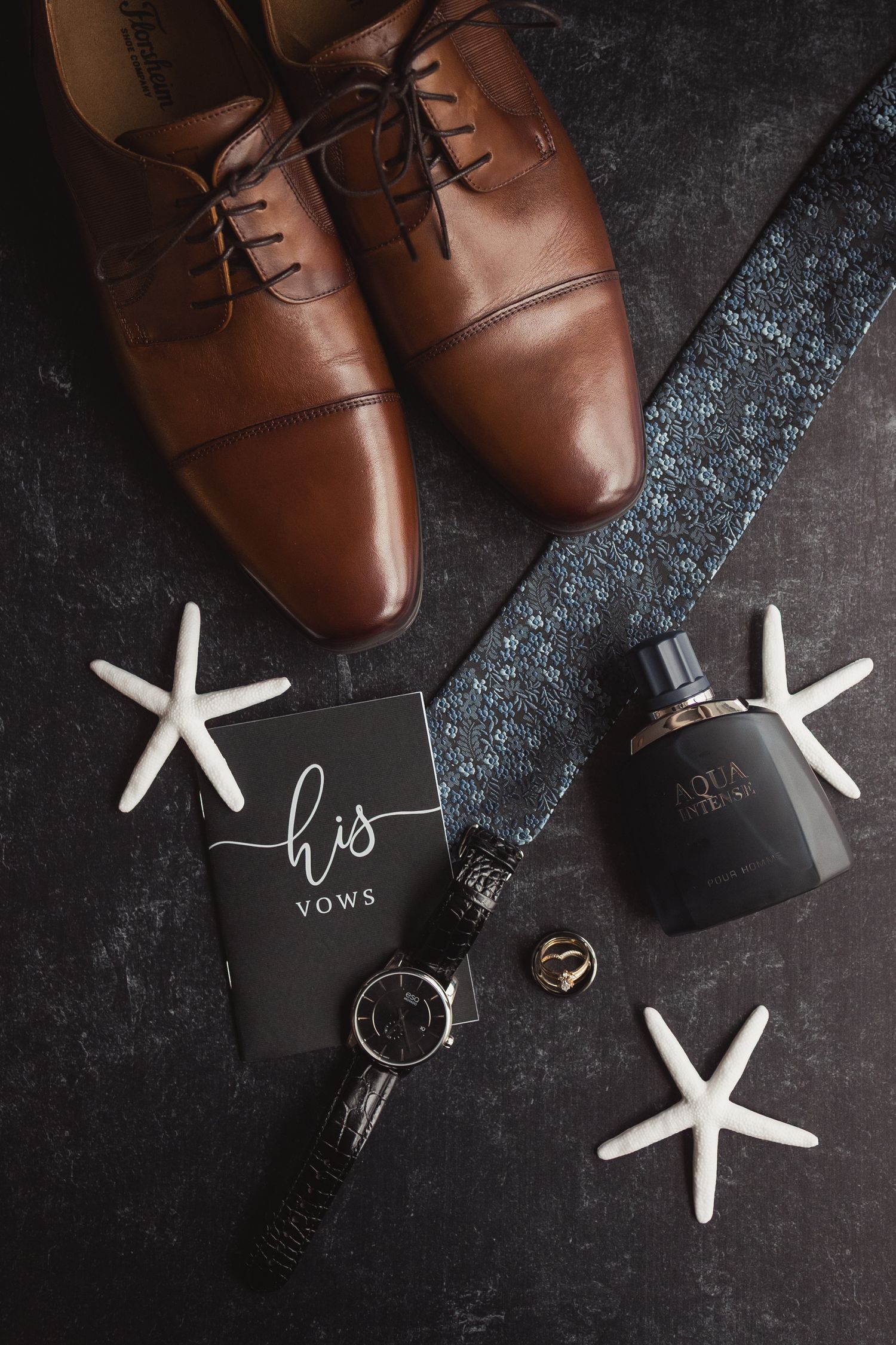 Brown leather dress shoes with wedding accessories and starfish decorations on dark surface.