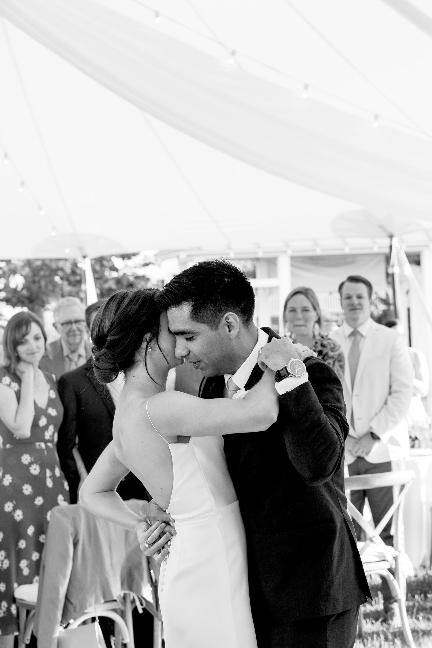 A romantic black and white photo of a couple sharing a tender moment at an outdoor wedding celebration.