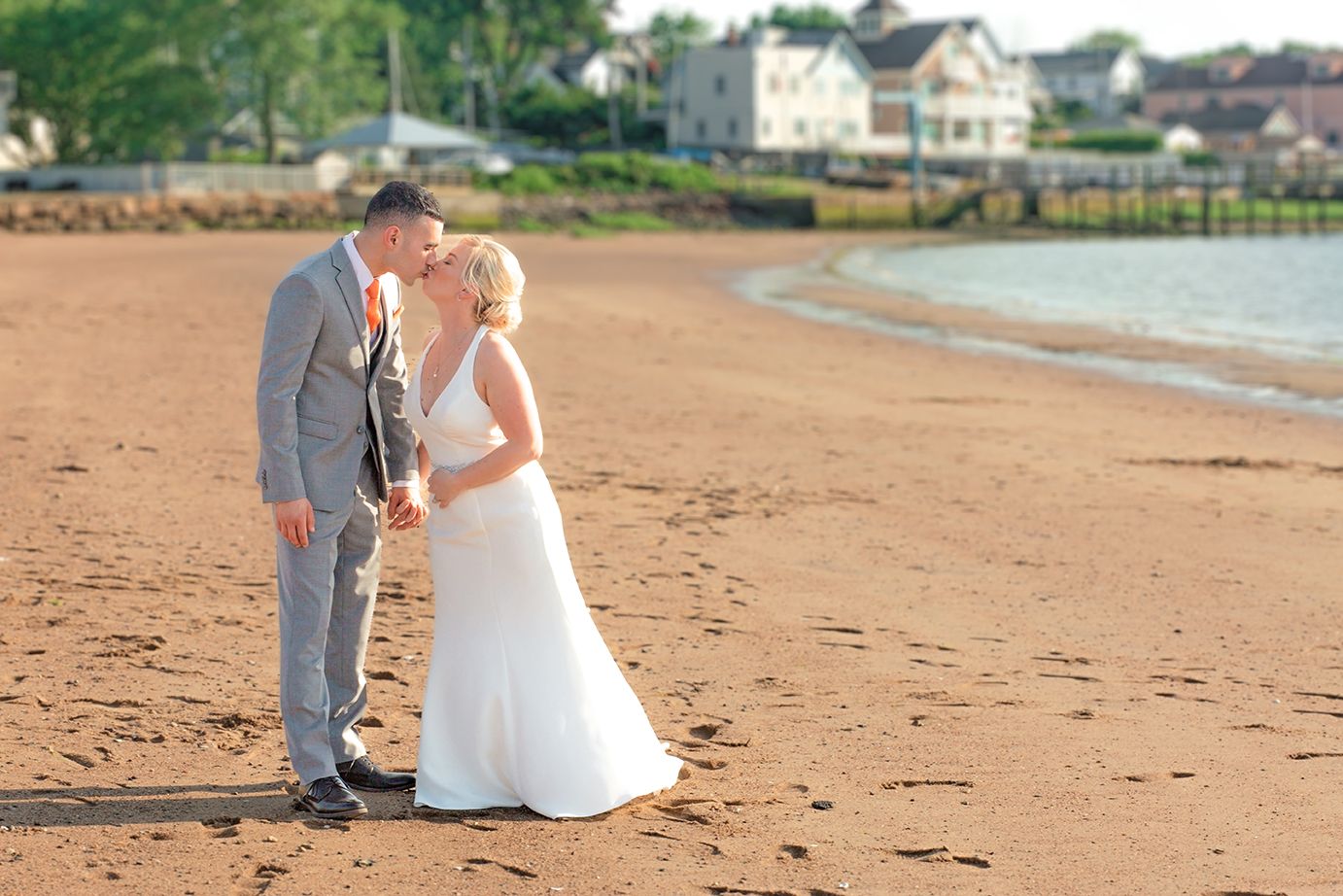 Couple in wedding attire walking together on a sandy beach during golden hour.