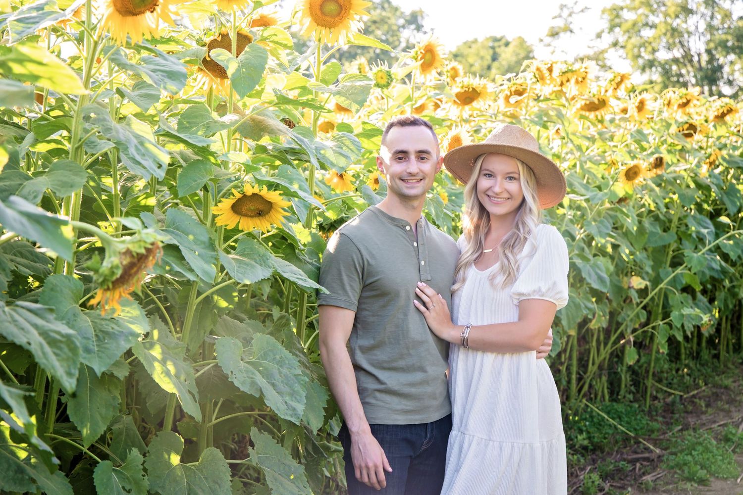 A couple poses together in a vibrant sunflower field on a sunny summer day.