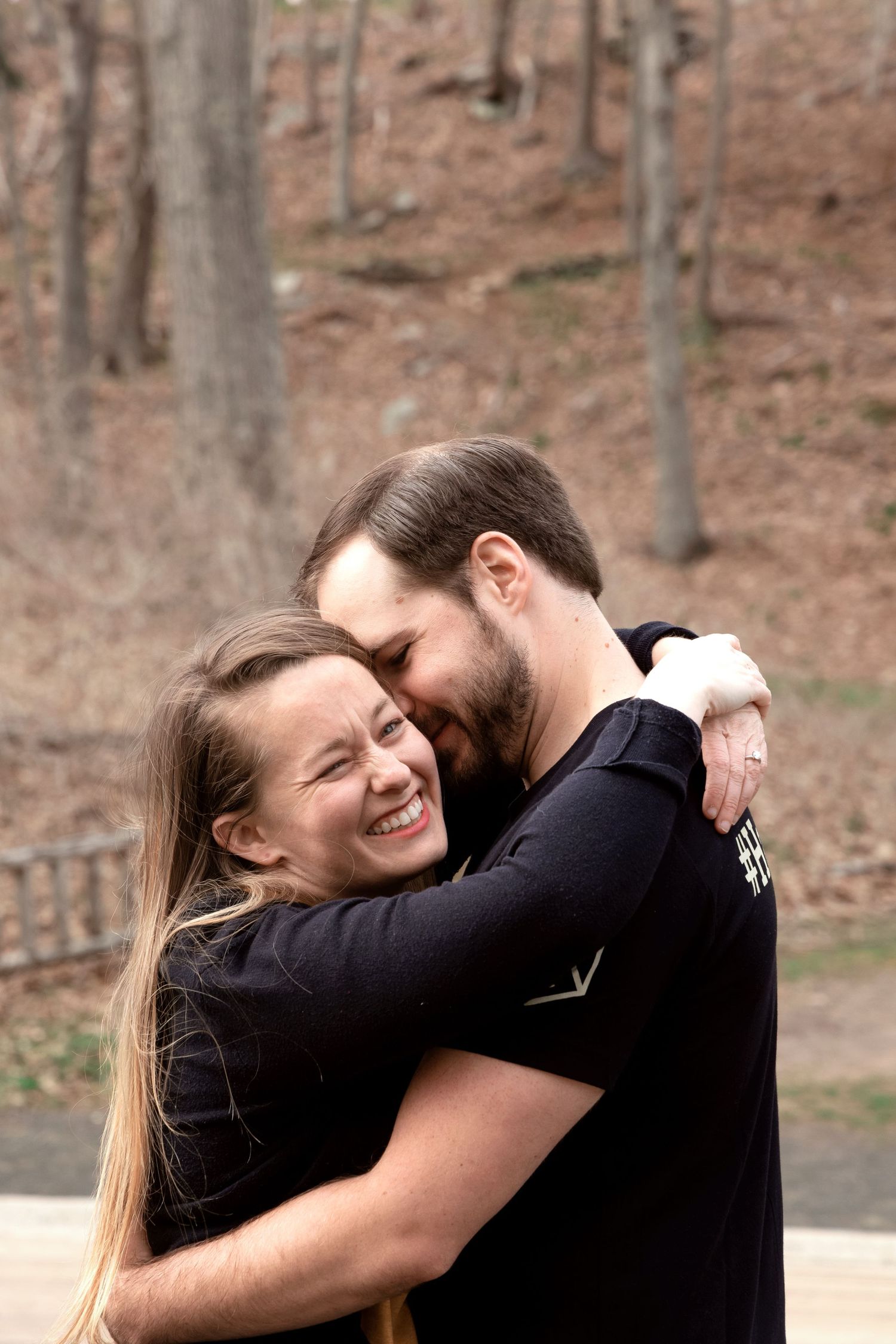 A joyful couple embraces and laughs together in front of a wooded forest background.