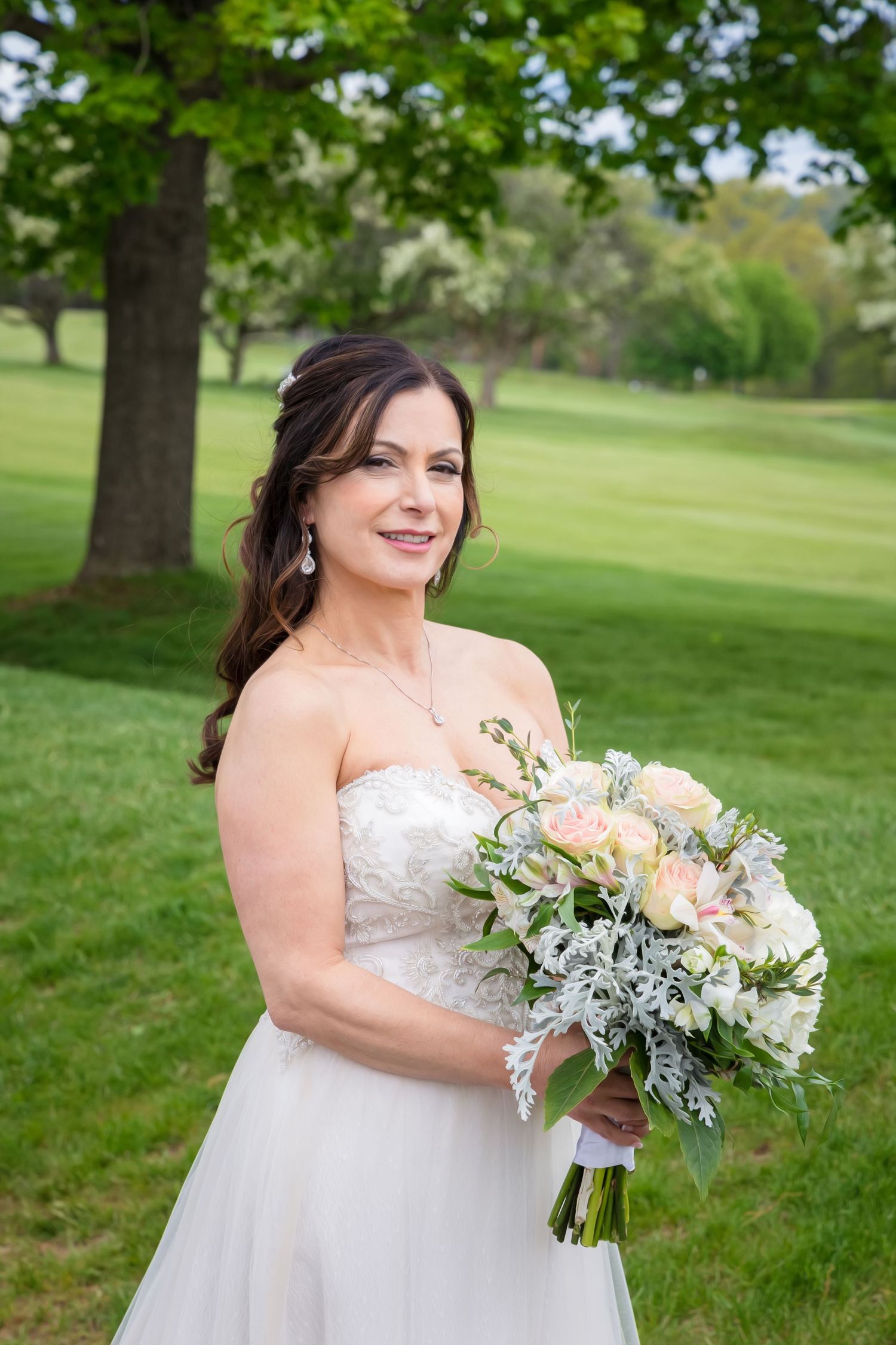 Beautiful bridal portrait outdoors holding a romantic bouquet with blush roses and silvery greenery in a garden setting.