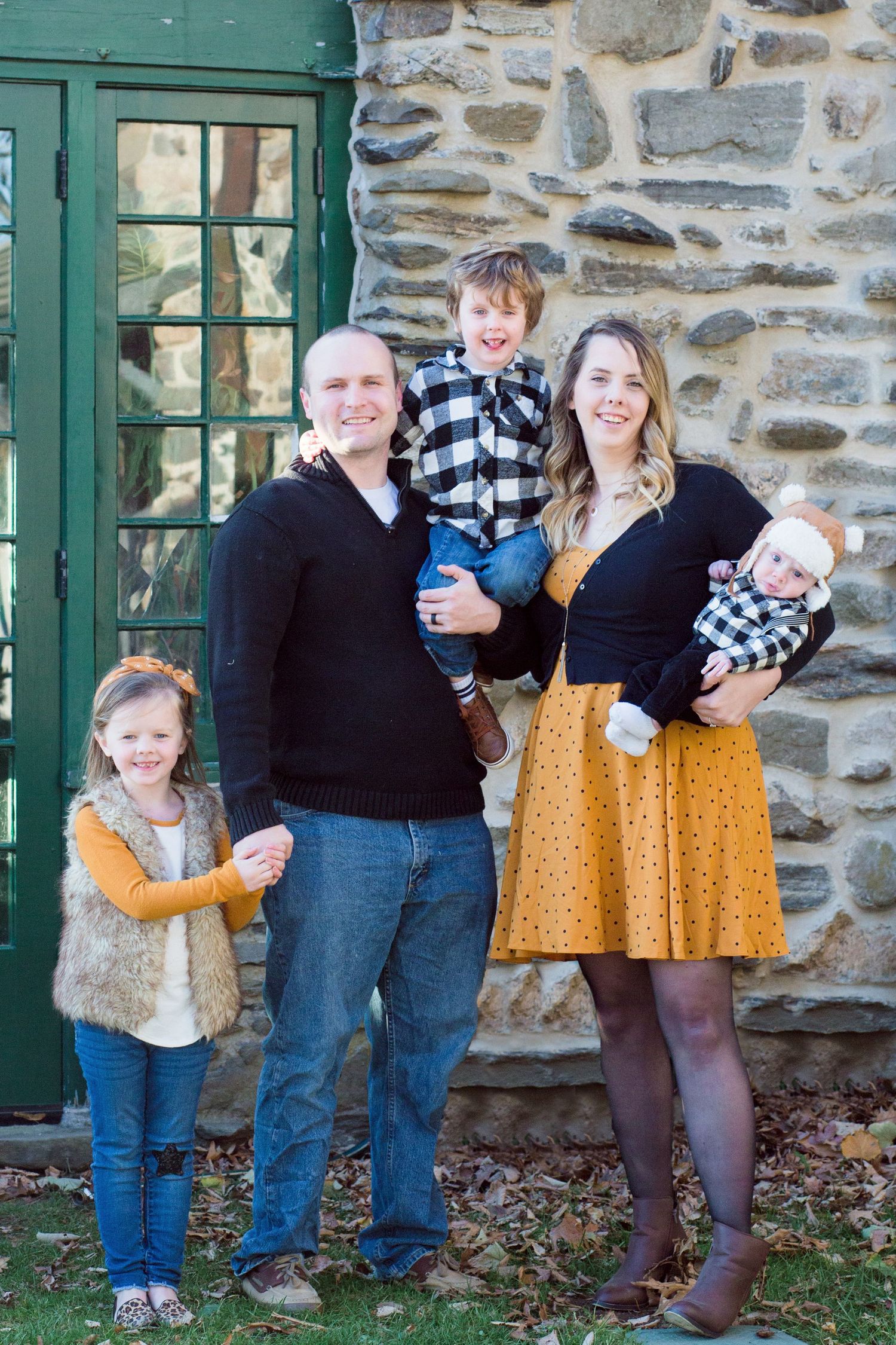 Four progressive family photos show playful poses against a rustic stone wall with green trim windows.