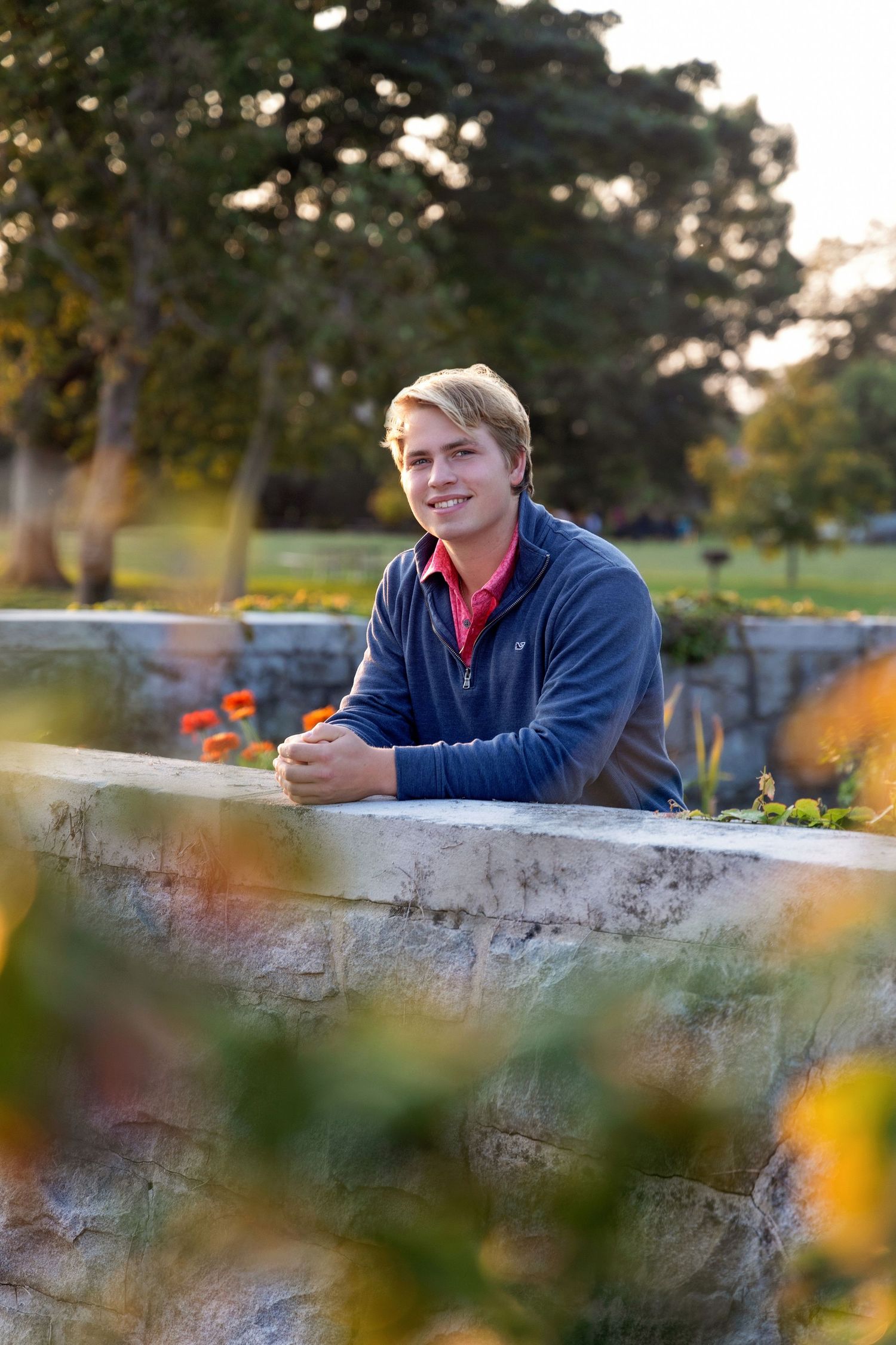 Outdoor senior portrait with stone wall and sunset lighting.