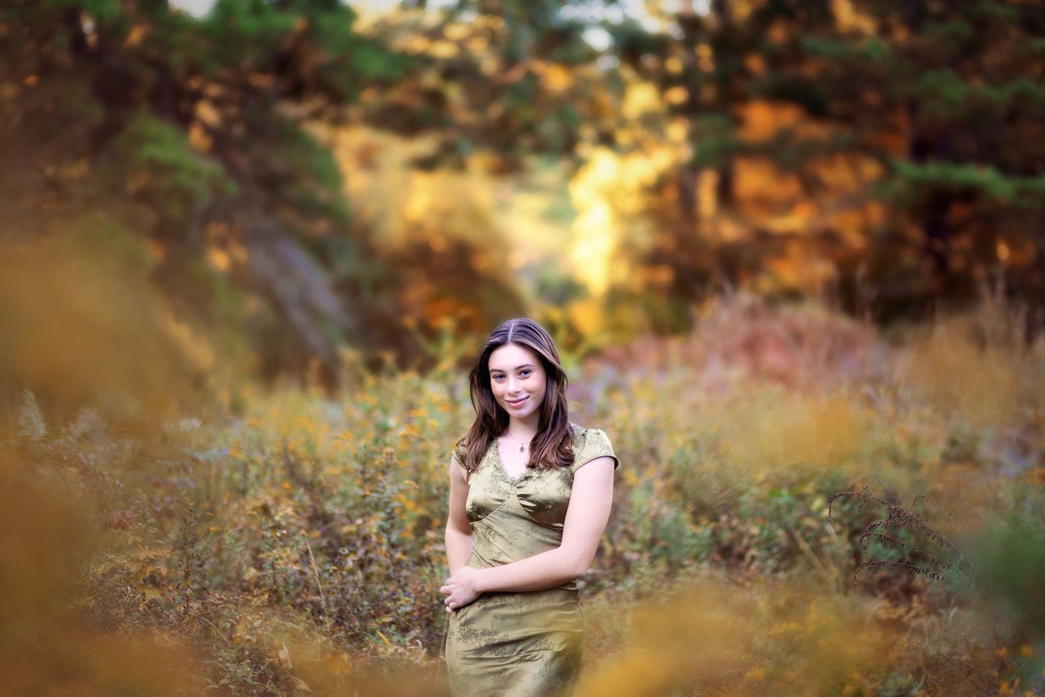 A person in a purple dress poses among autumn foliage during a golden hour outdoor photoshoot.