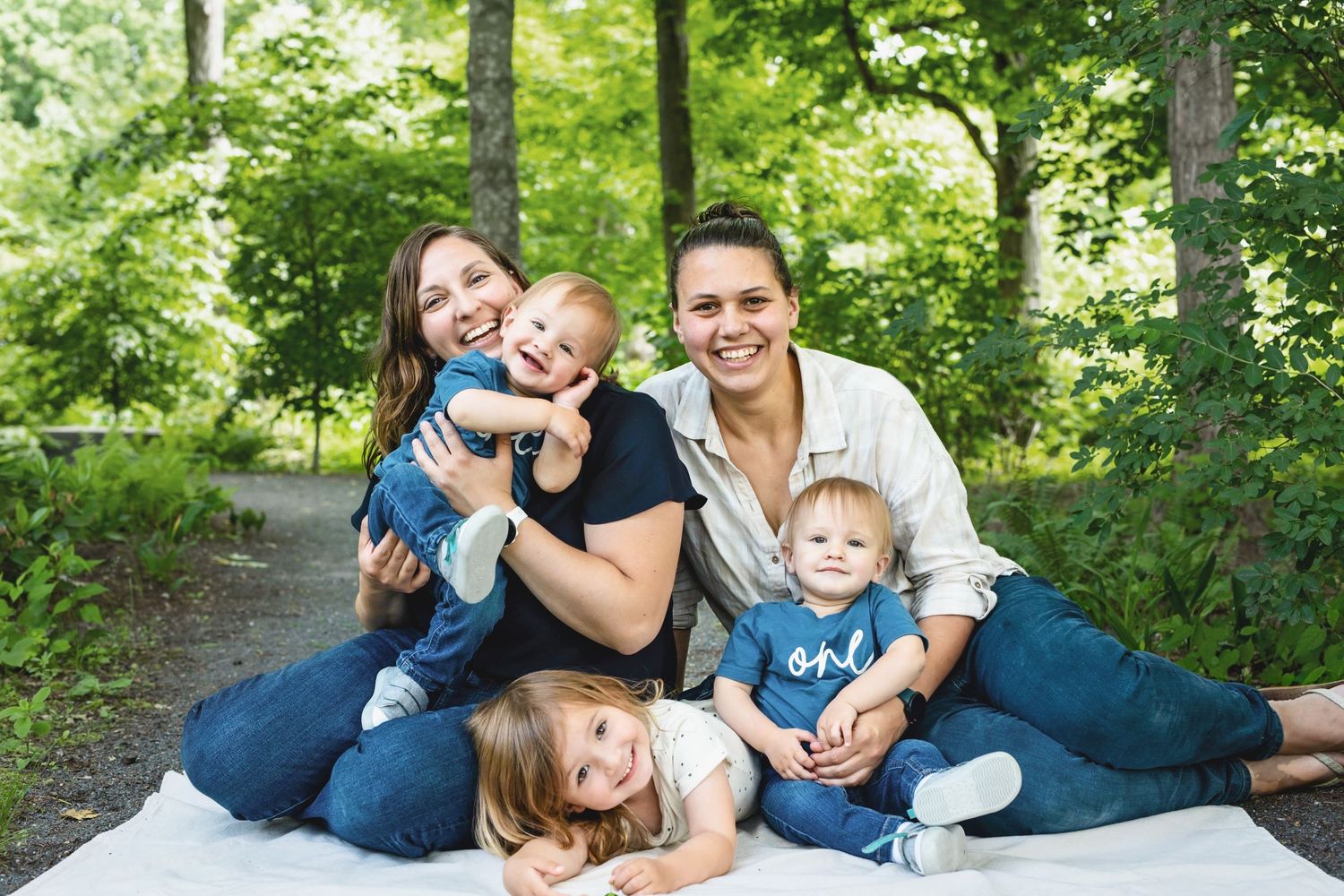A group sits together in casual clothing on a wooded path during an outdoor photo session.