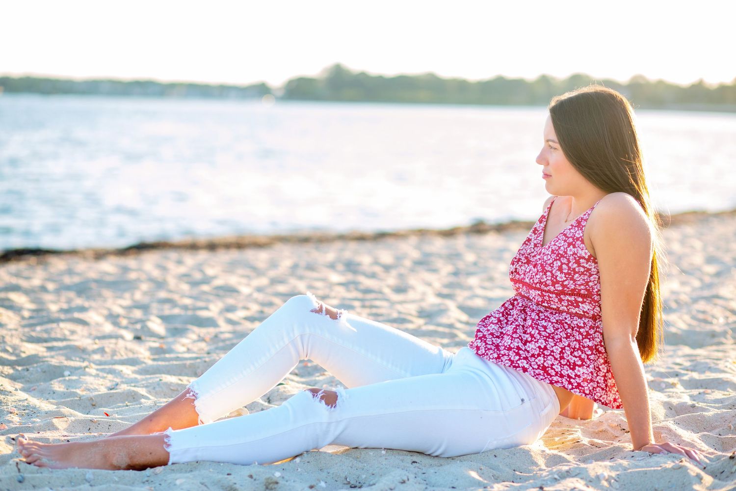 Person in pink floral dress relaxing on sandy beach during golden sunset hour.
